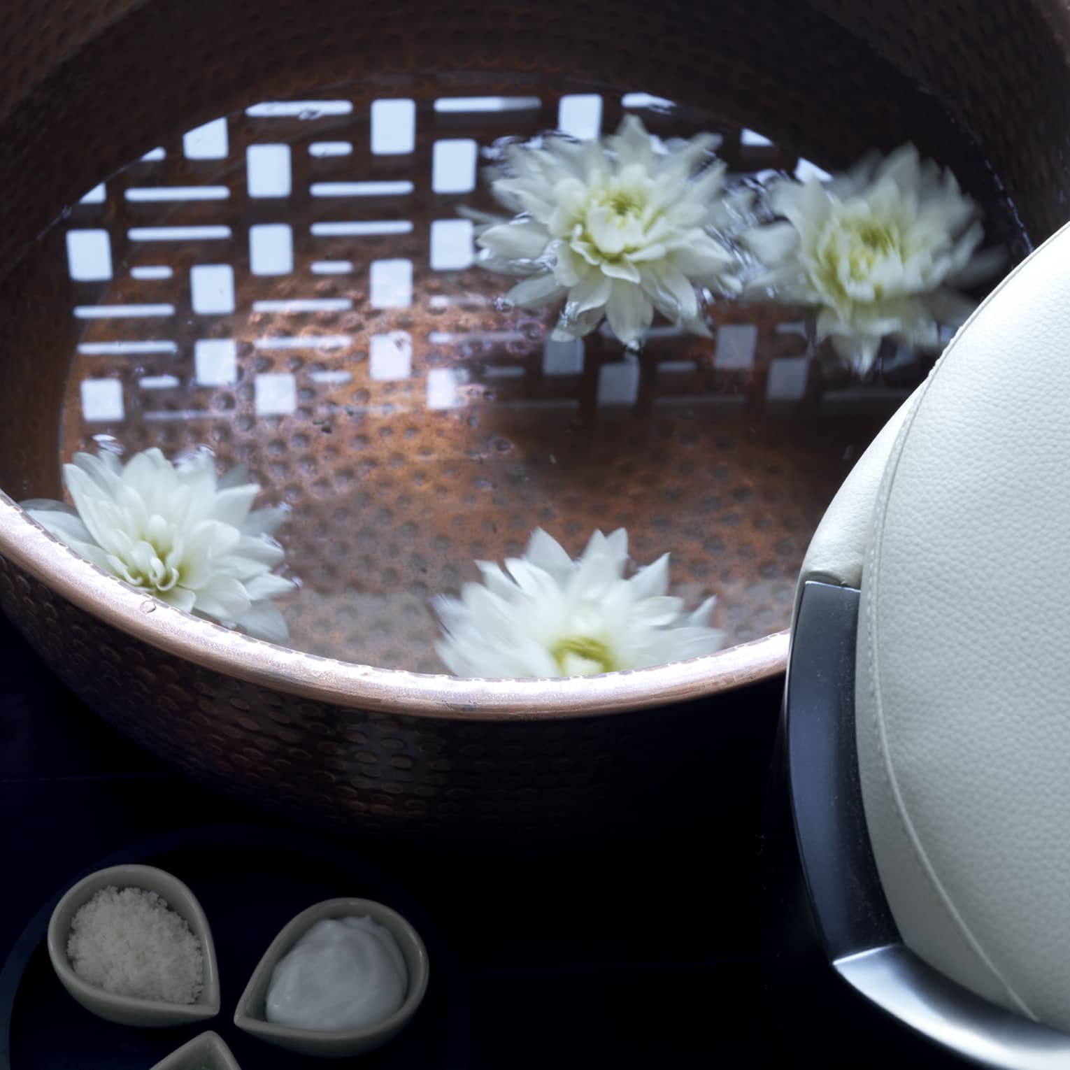 Close-up of copper bowl with water, floating white flowers, small dishes with spa salts, oil and lemons