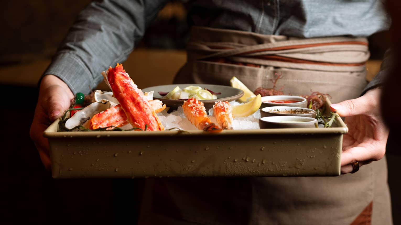 A person holds a tray containing food items and sauces on ice.