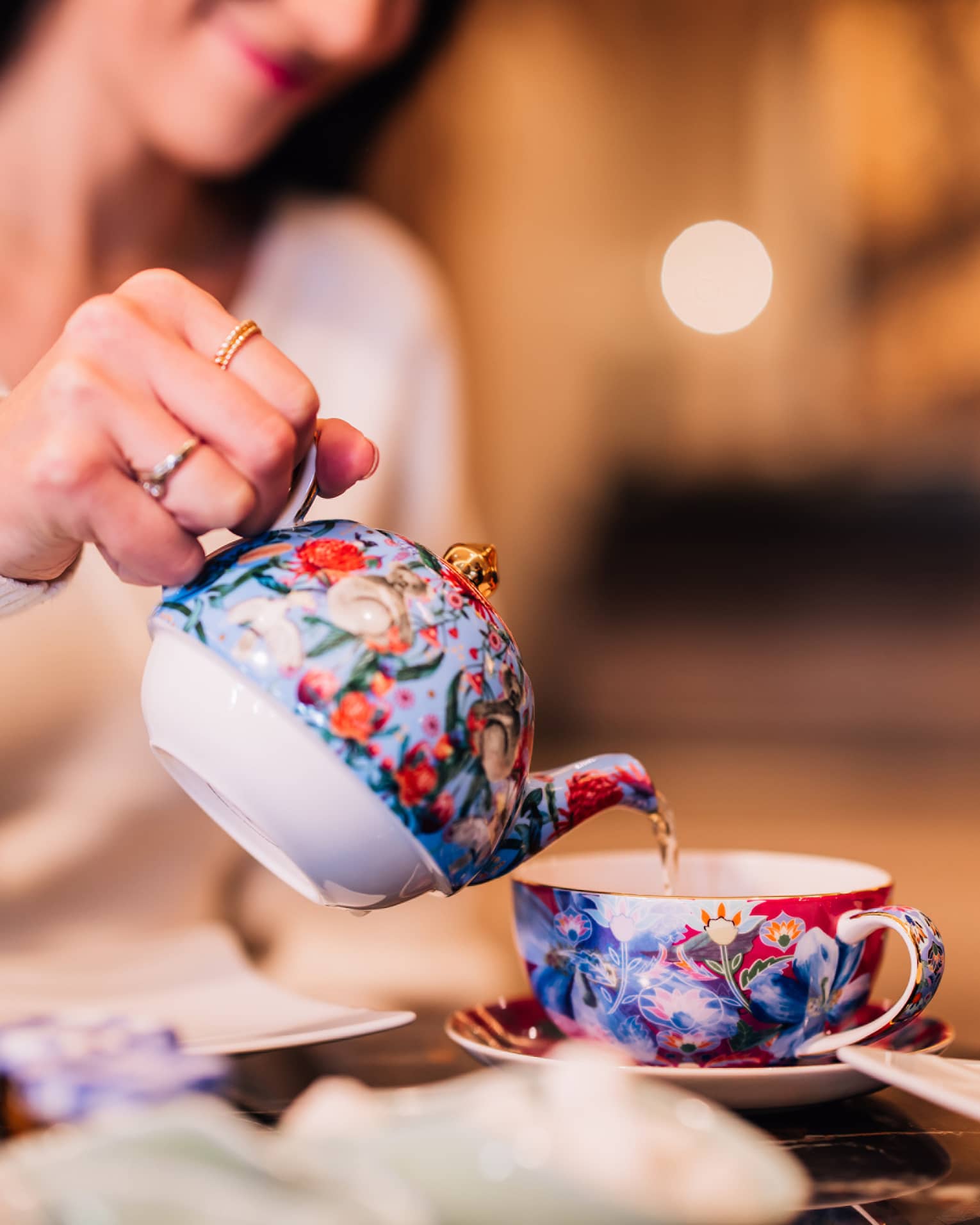 A woman pouring tea out of a colourful kettle.