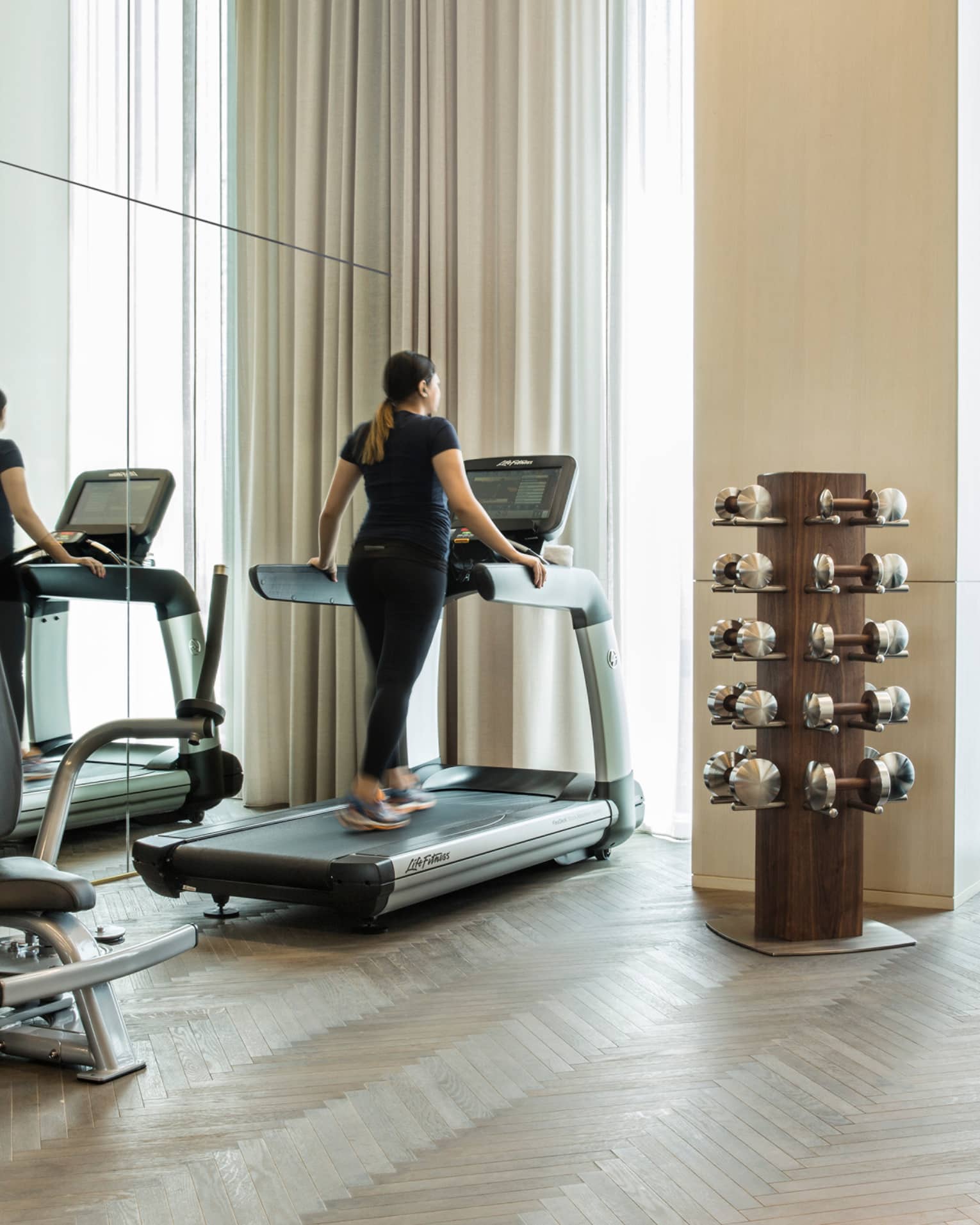 Woman walks on treadmill beside mirror wall