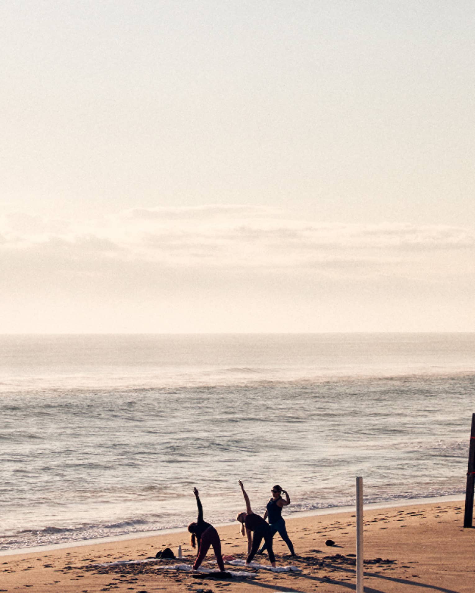 Three guests doing yoga on the shore of the beach with the ocean in the background.