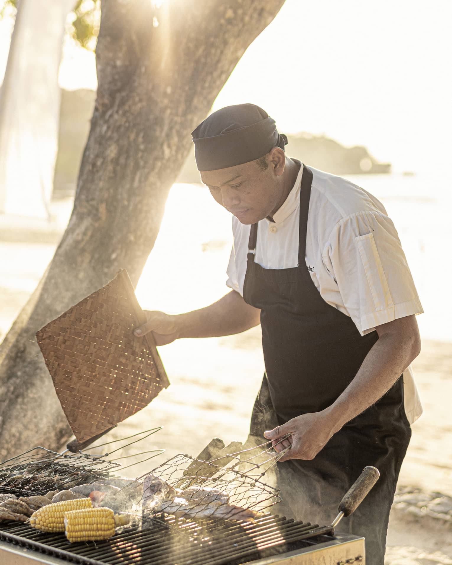 Chef grills fresh clams and corn on the cob over a beachside BBQ