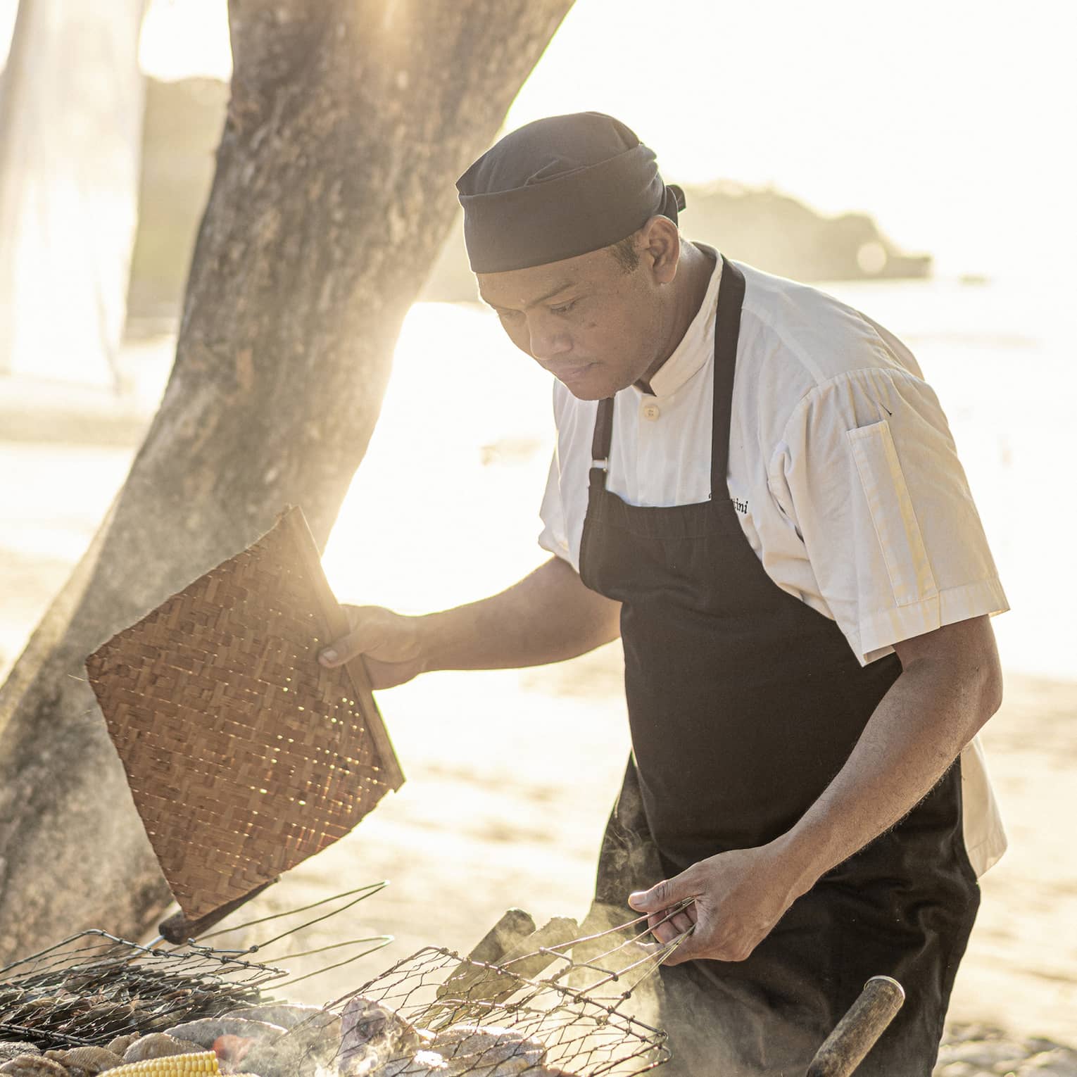 Chef grills fresh clams and corn on the cob over a beachside BBQ