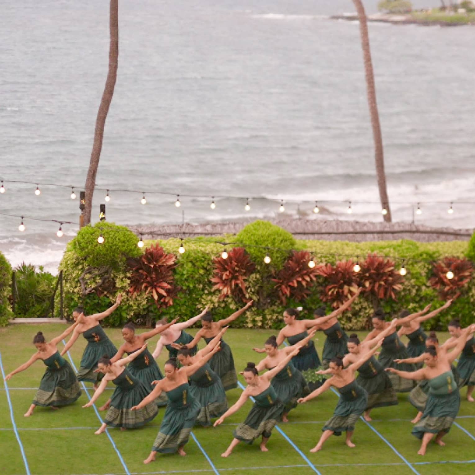 A group of hula dancers perform on an oceanside lawn at luxury resort