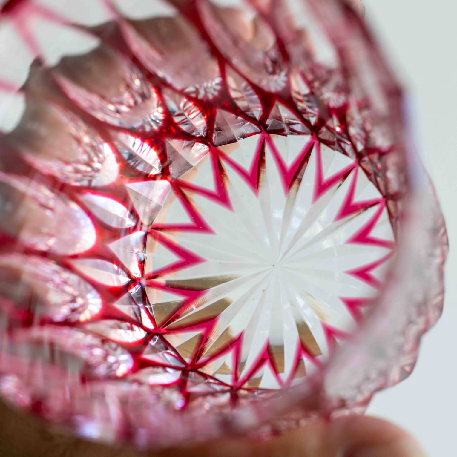 Extreme close-up inside a bright-red cut glass tumbler with a starburst base and intricate geometric patterns on the sides.