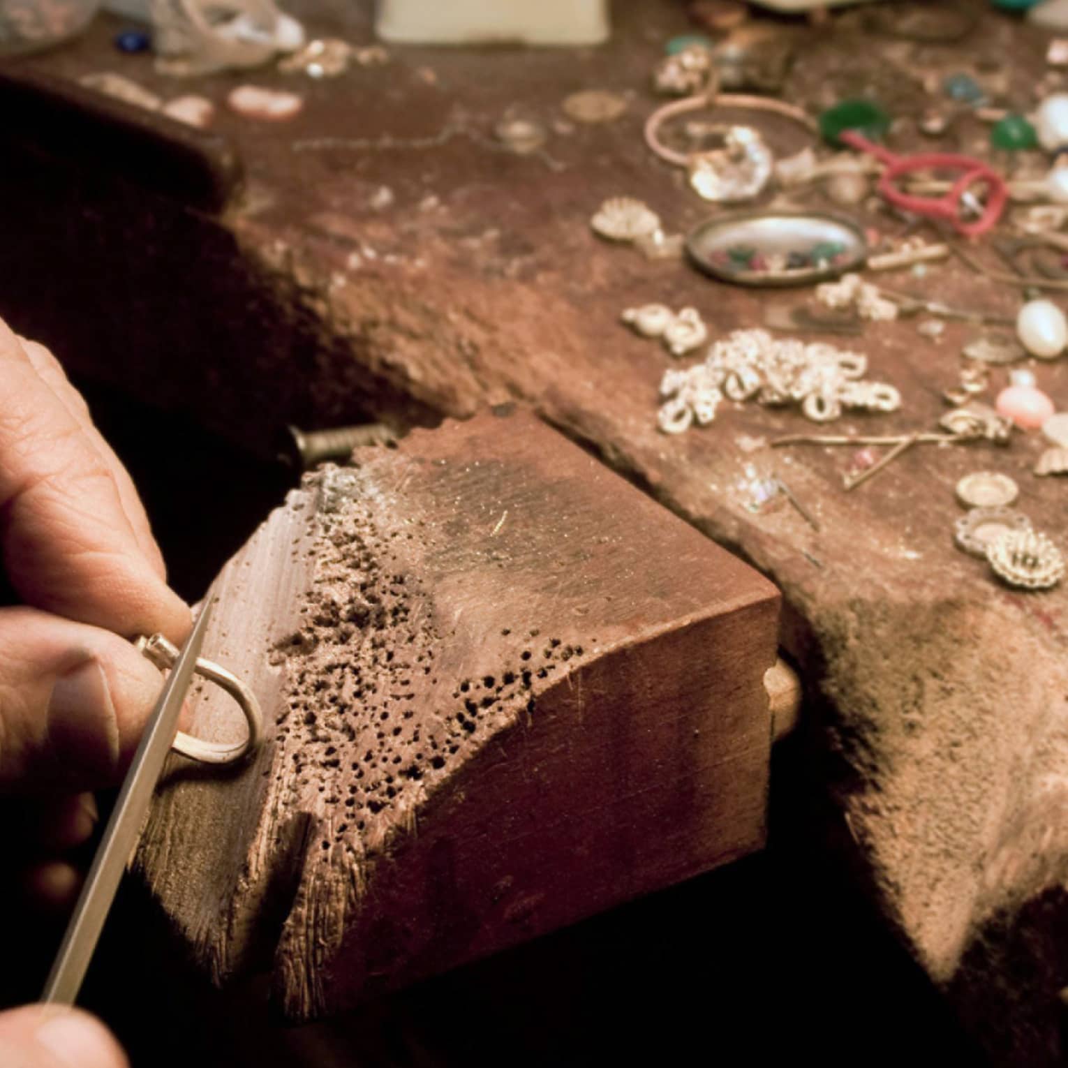 Jeweller's hands using a tool to craft jewellery on a wooden block
