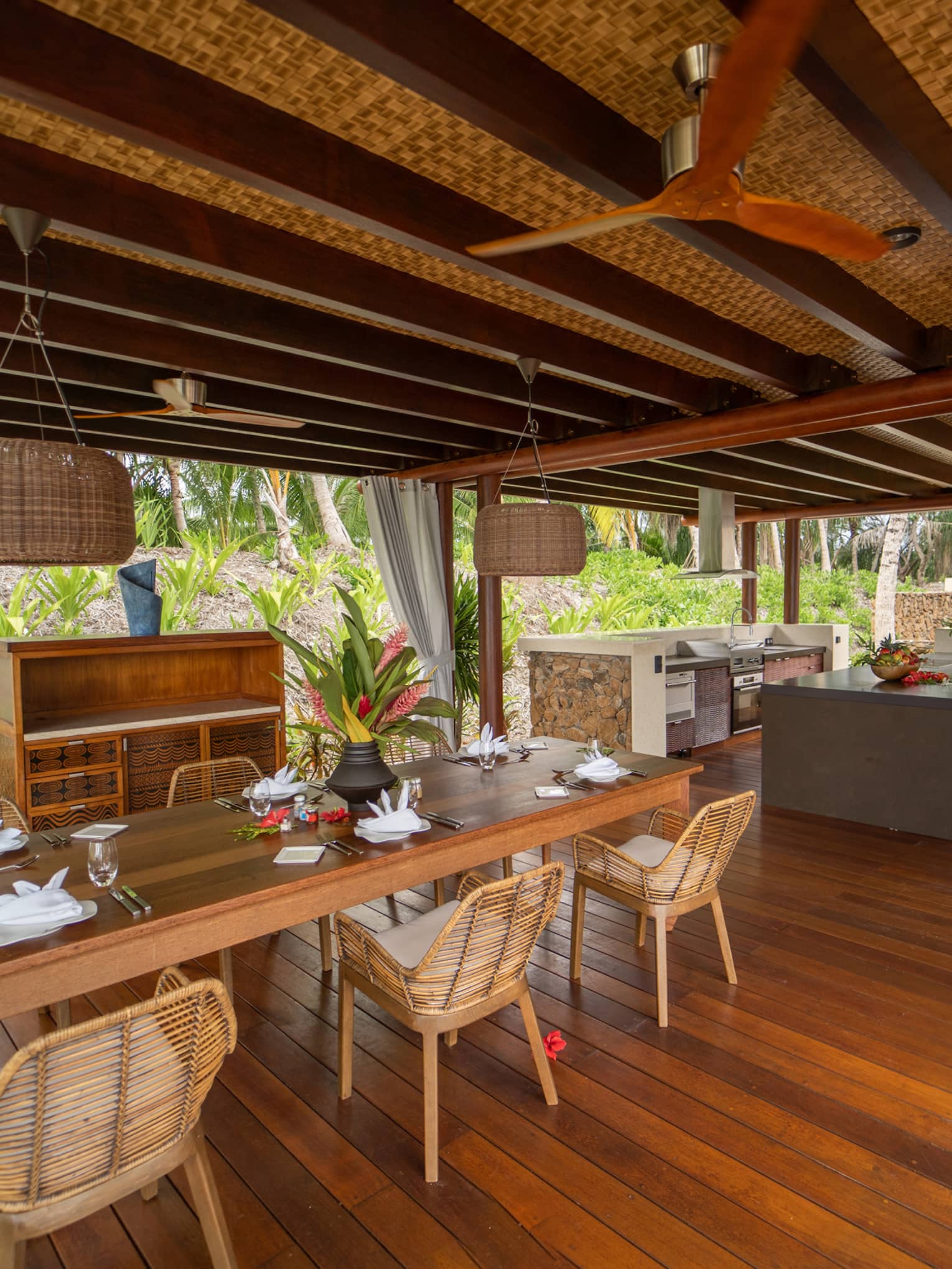 Open-air dining area with wooden floors, bamboo chairs, thatch roof