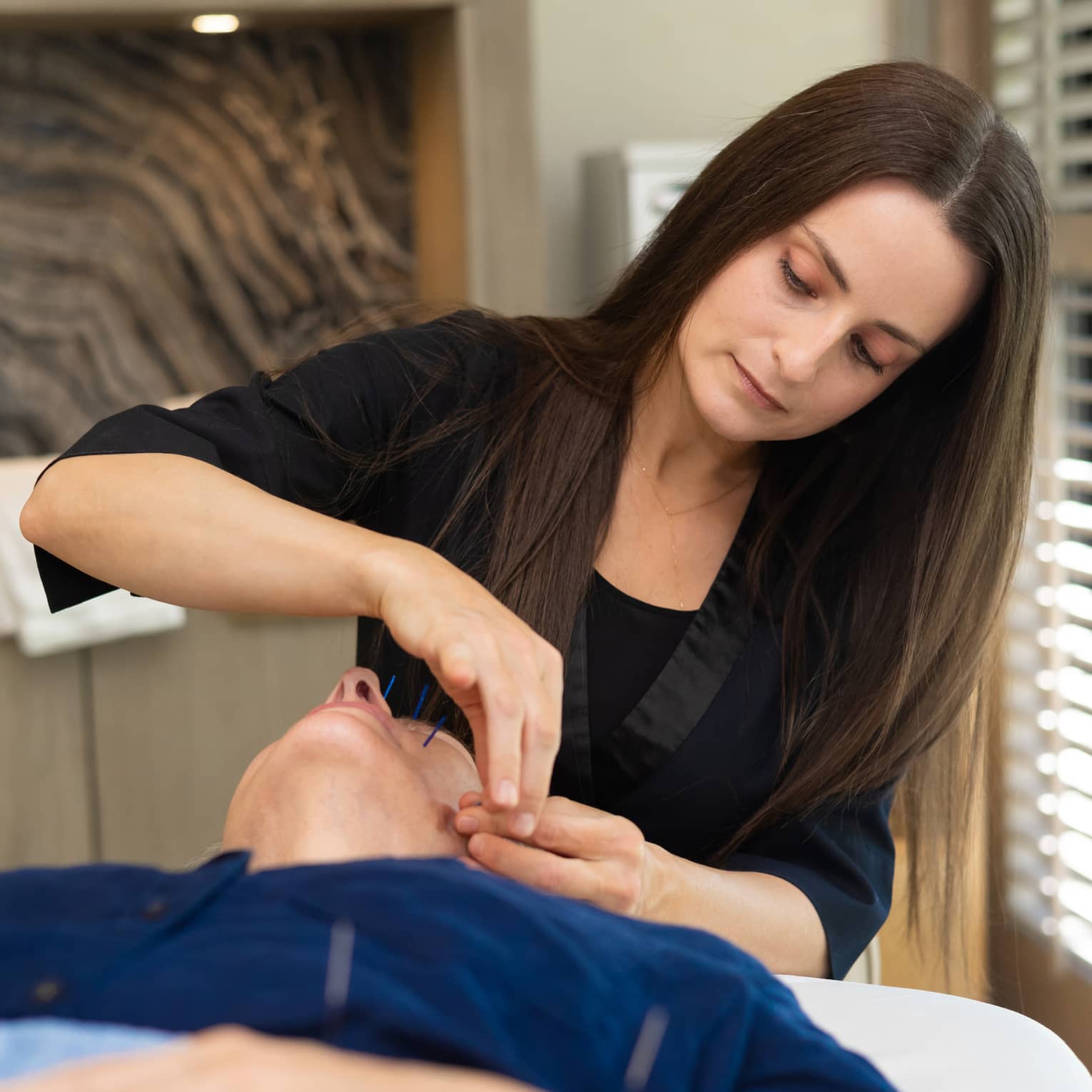 Woman performs acupuncture on person's face at luxury resort spa