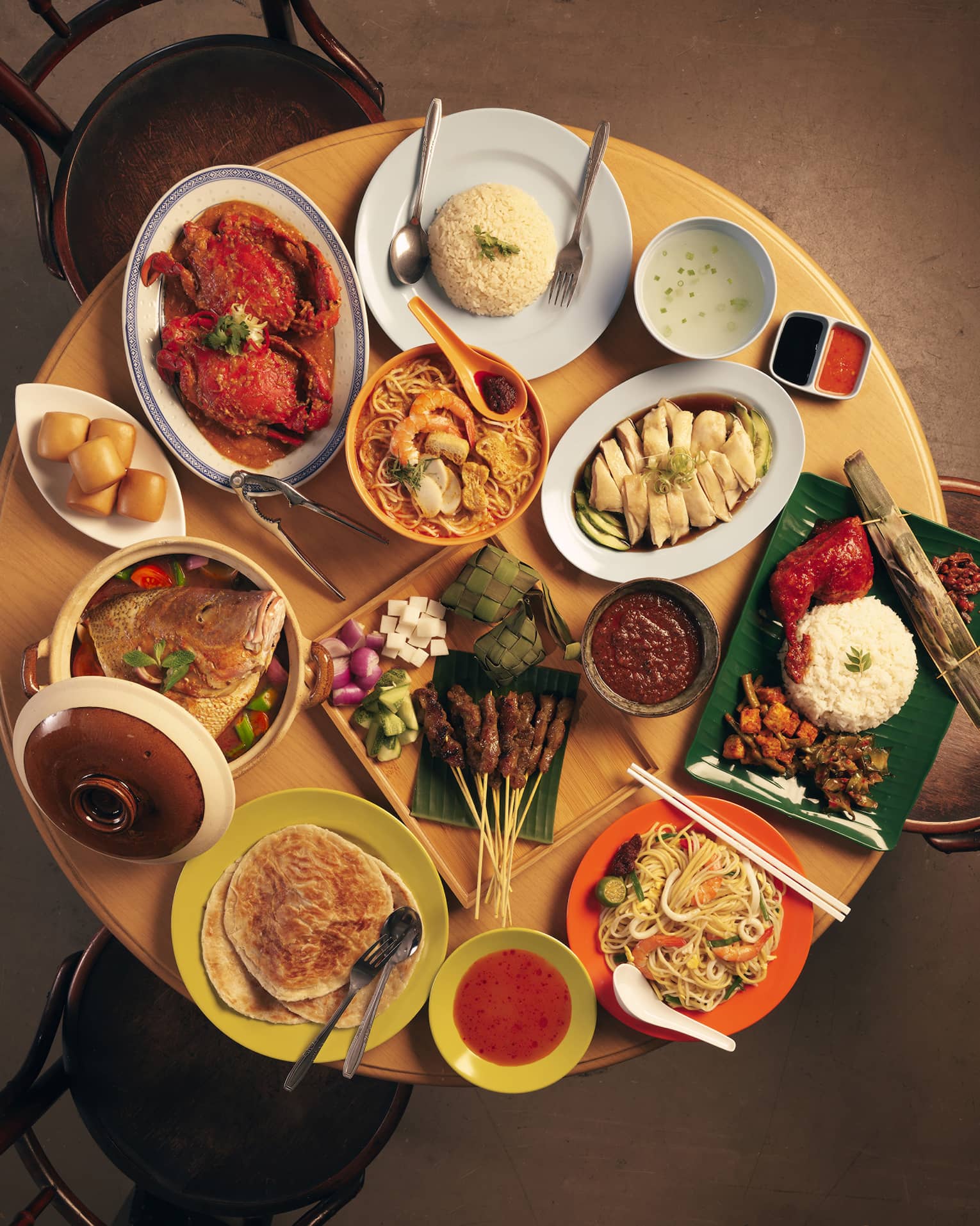 Overhead view of a round table covered in colourful dishes of crab, prawns, chicken, noodles, rice, skewers and flatbread