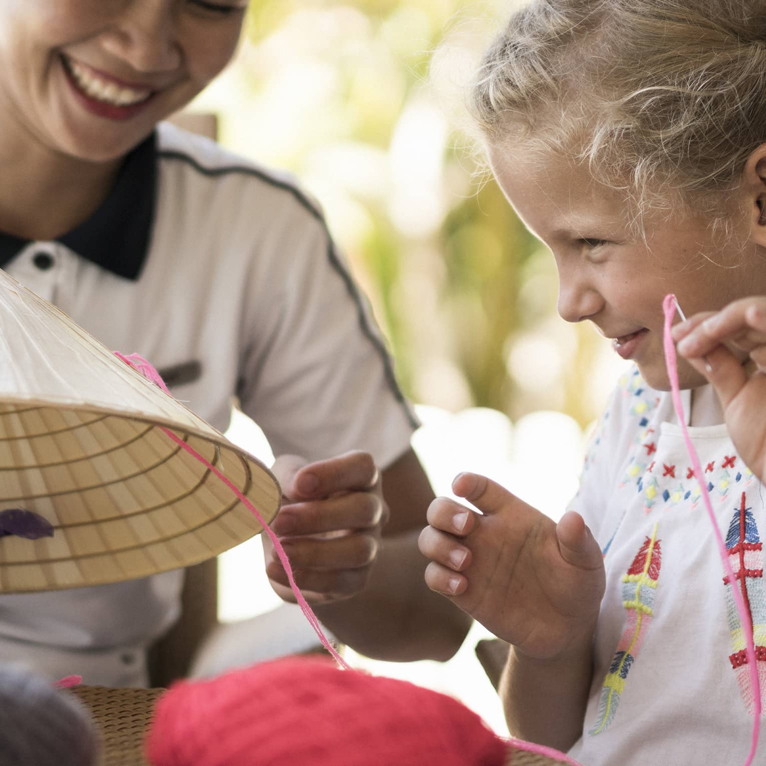 Hotel staff helps young girl thread string on traditional hat