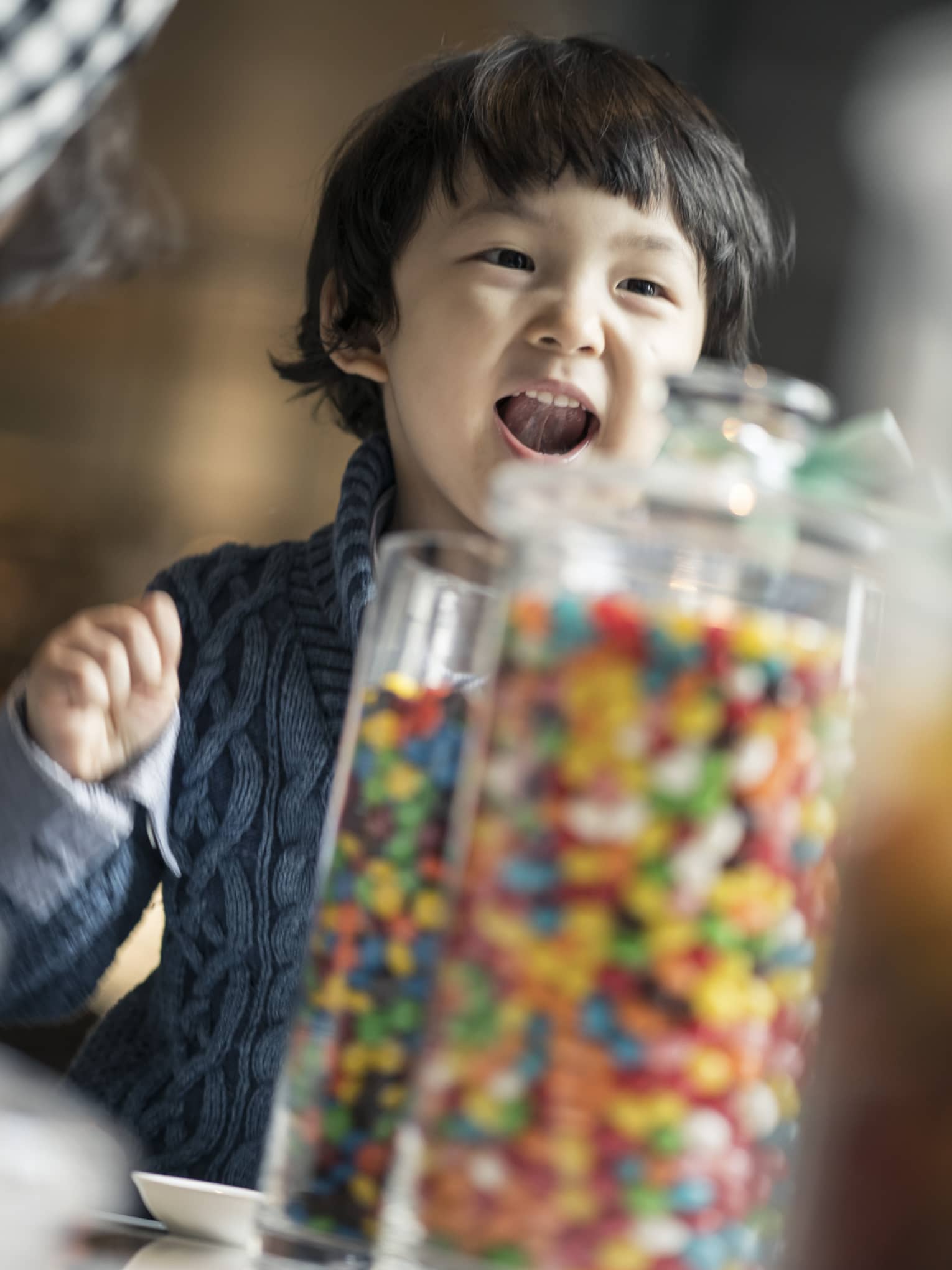 Toddler boy squeals in excitement at the sight of glass jars filled with sweets