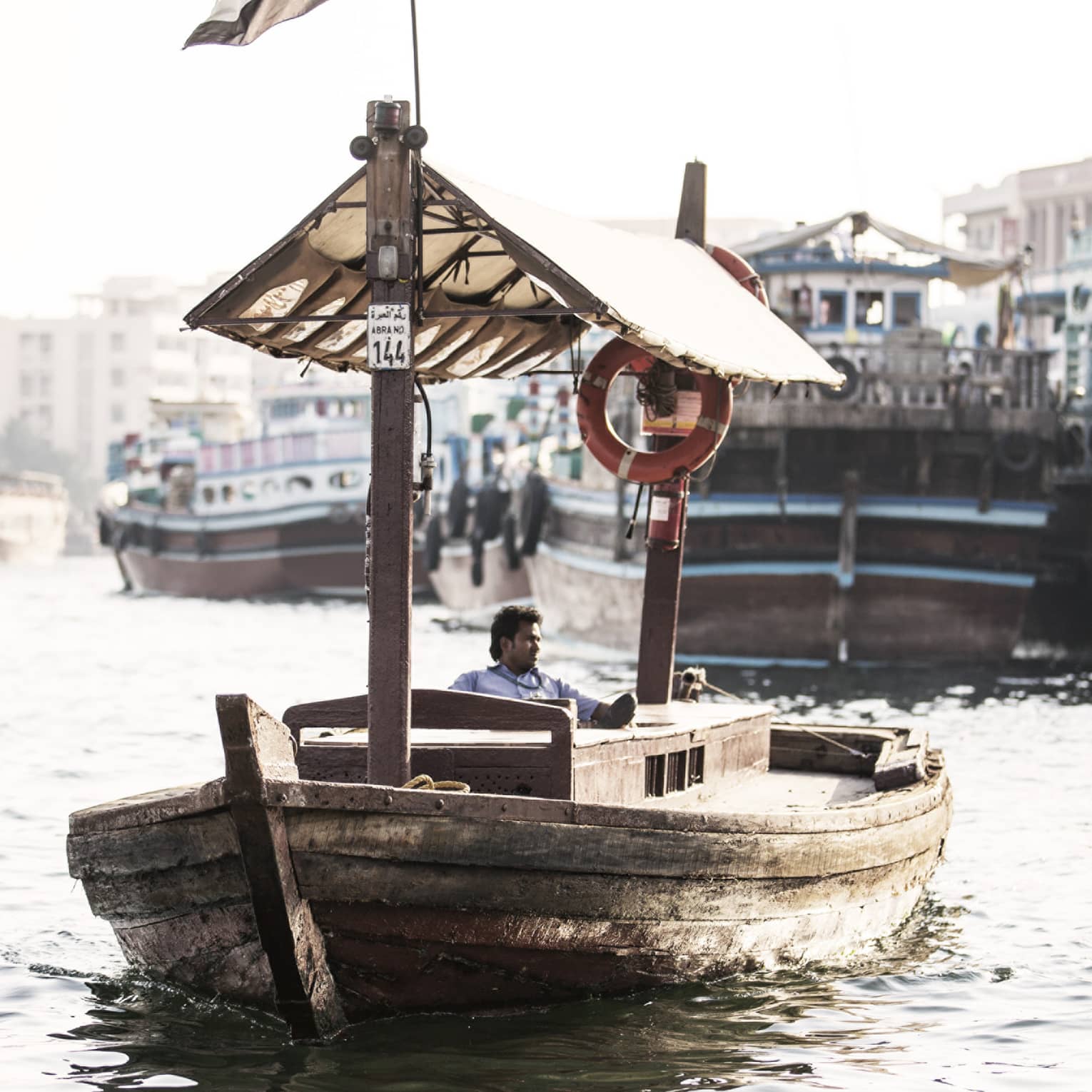 A small wooden boat flying the UAE flag as it sails down a small waterway. 