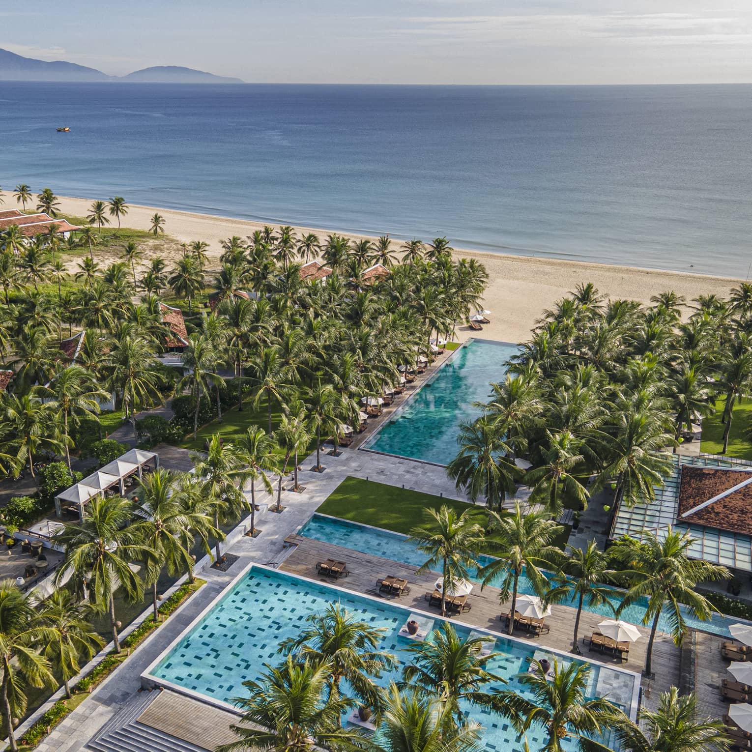 Aerial view of the resort pools with ocean views, palm trees and blue skies