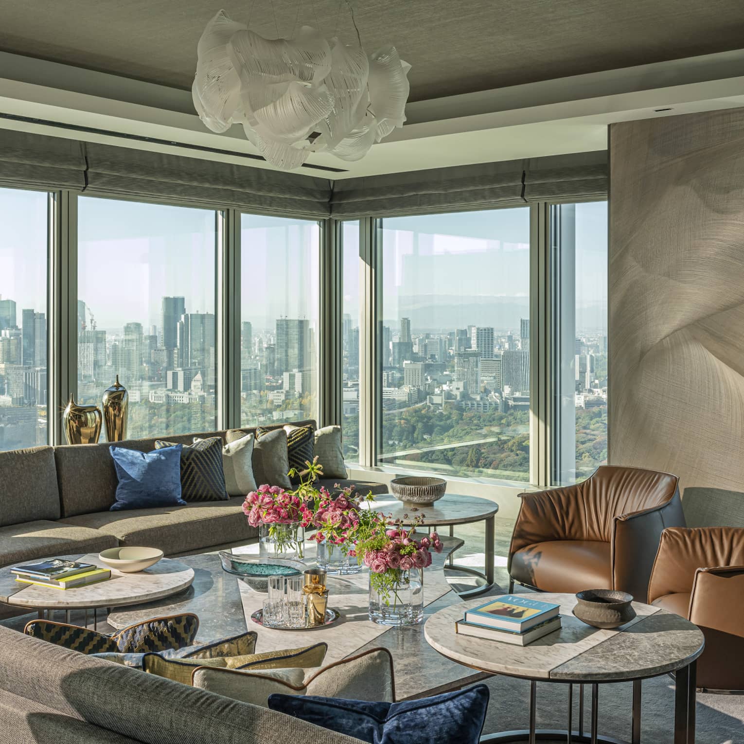 Luxury imperial hotel suite with large sectional sofa, leather armchairs, multiple coffee tables and floor-to-ceiling windows with panoramic city views