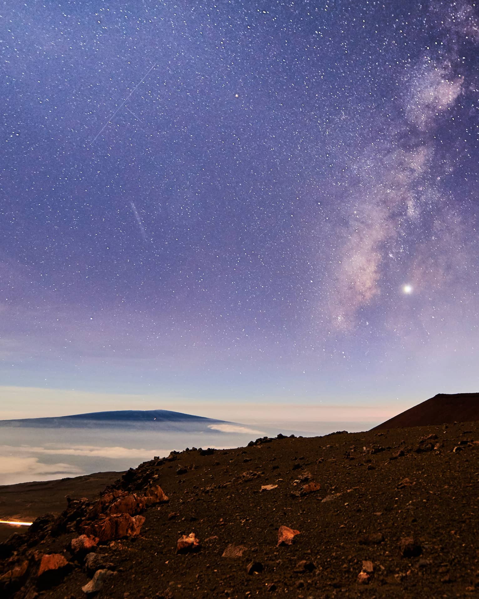 Sunrise under starry sky above mountain, volcanic rocks