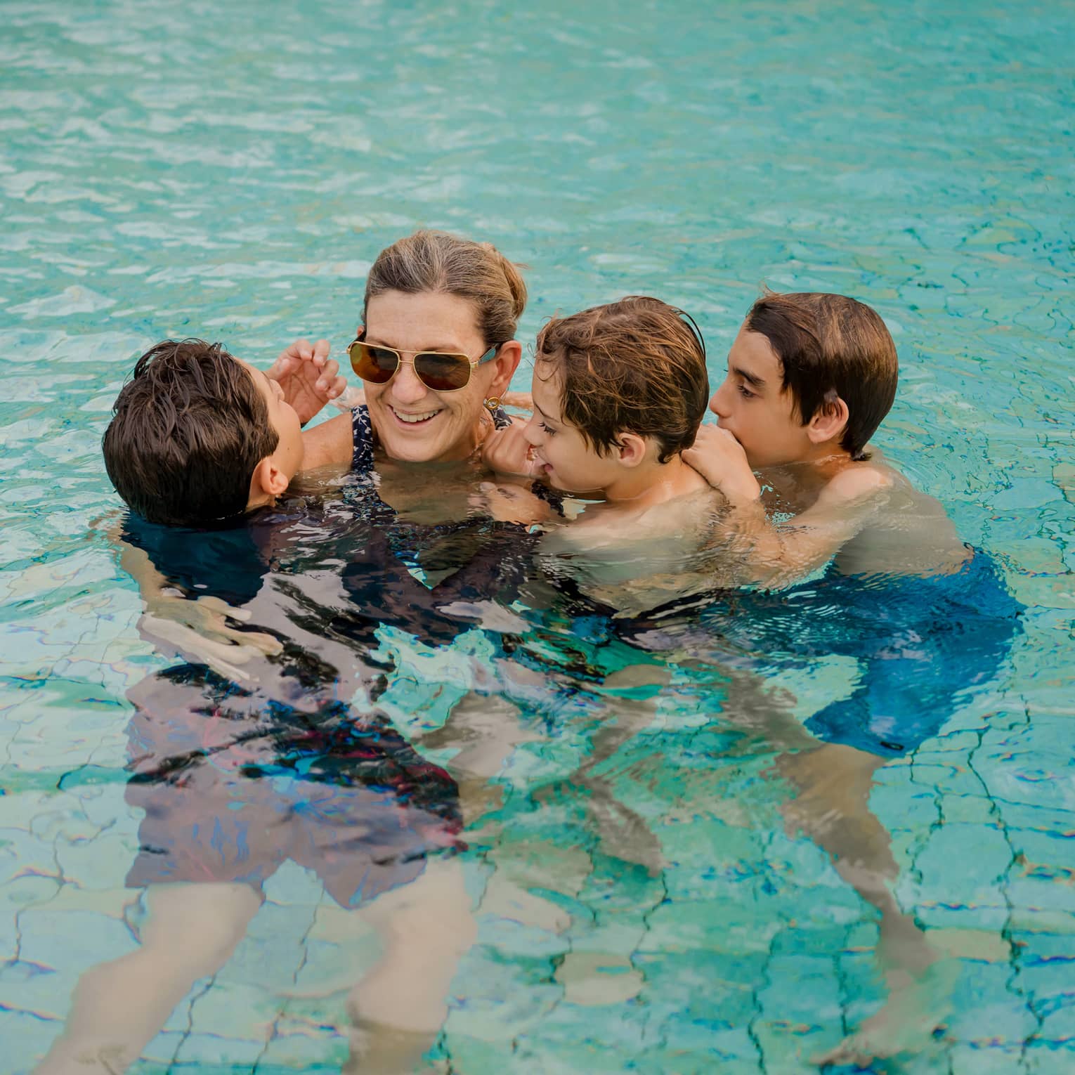 A mom and three children swim huddled together in a pool