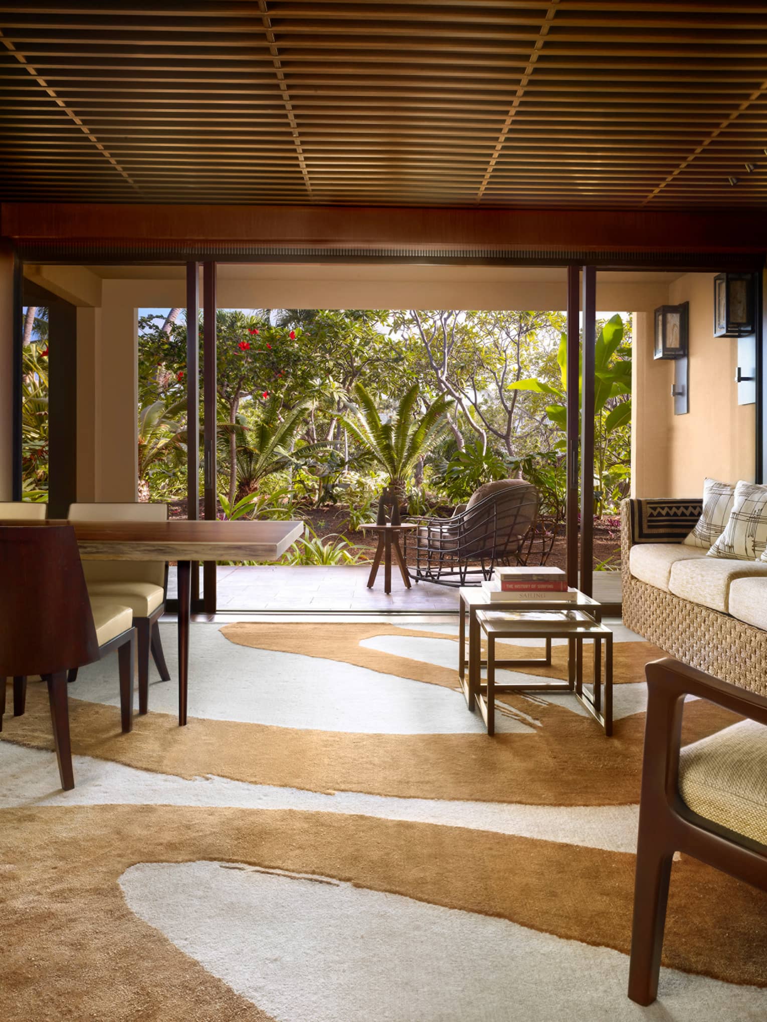 Ohana Garden-View Suite teak-panelled walls, wave screen over wood dining table, sofa, swirl-patterned carpet