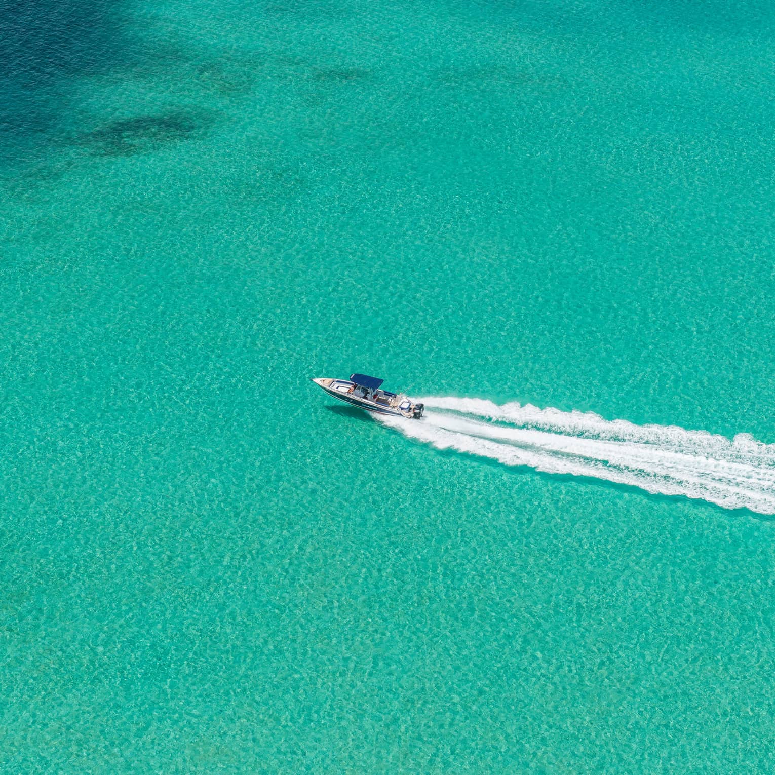 Aerial view of a speedboat moving through a vast expanse of turquoise water, followed by a substantial wake trail.