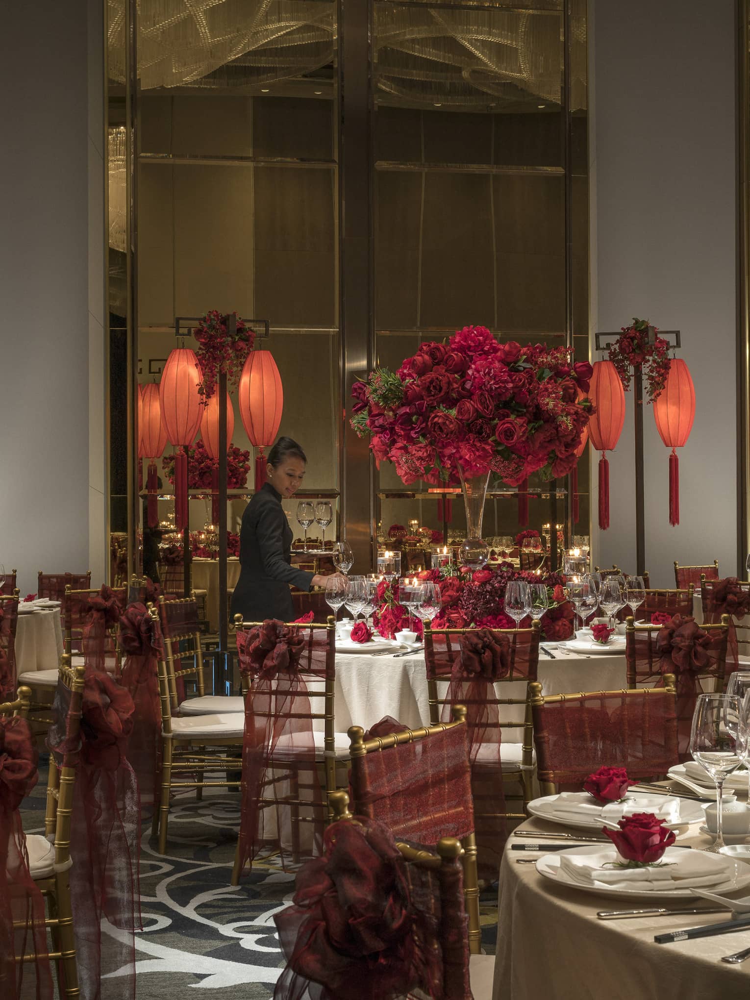 Hotel staff sets large round banquet tables with red flowers, lanterns for Chinese wedding