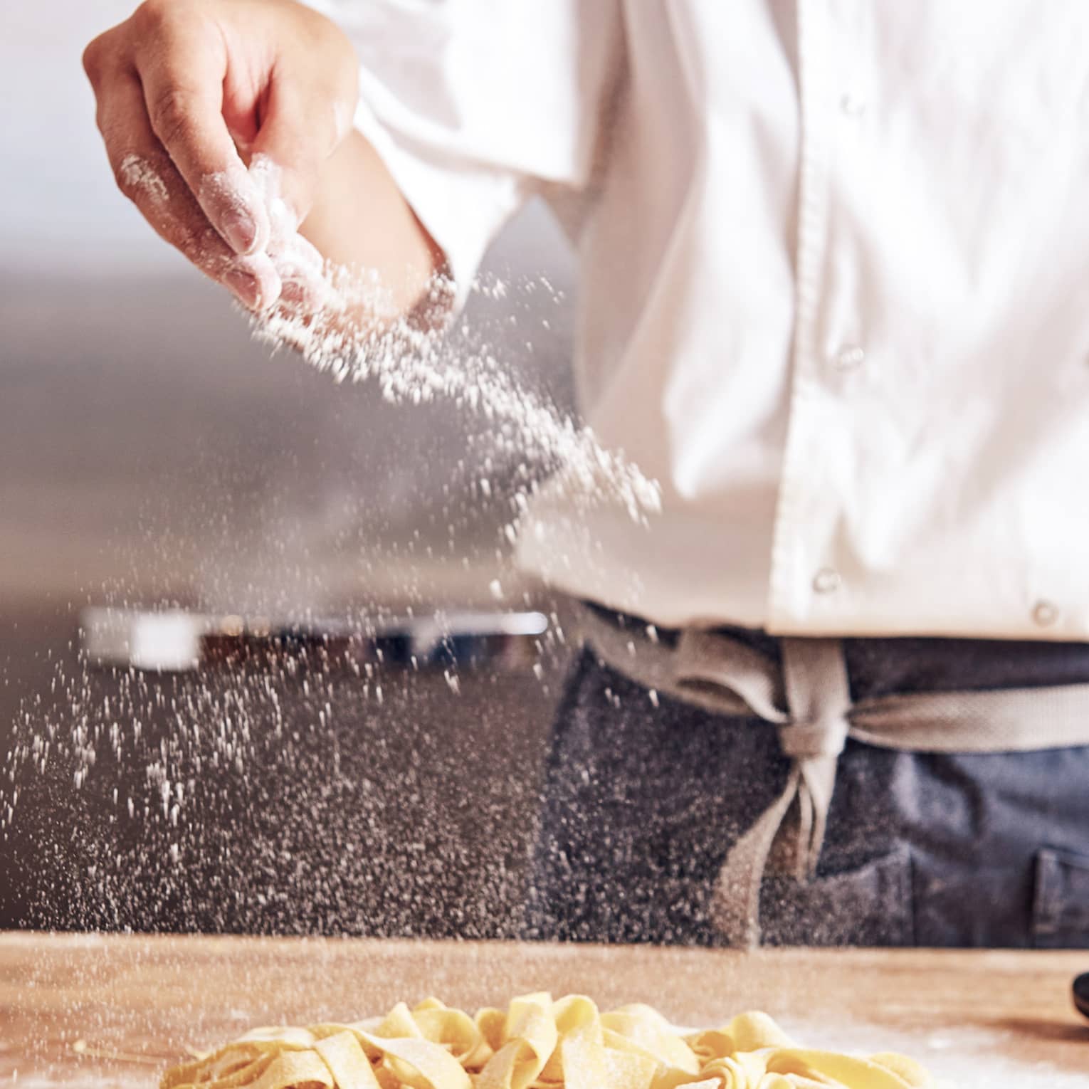 Noe chef sprinkles white flour over thick fresh pasta noodles on counter
