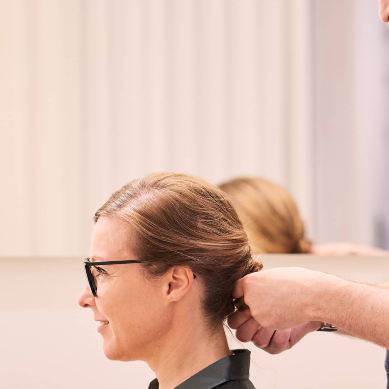 Woman sits in salon chair as hair stylist with long beard holds her hair
