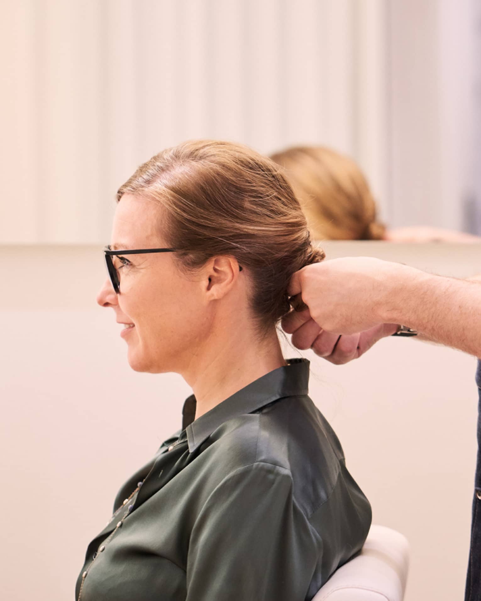 Woman sits in salon chair as hair stylist with long beard holds her hair