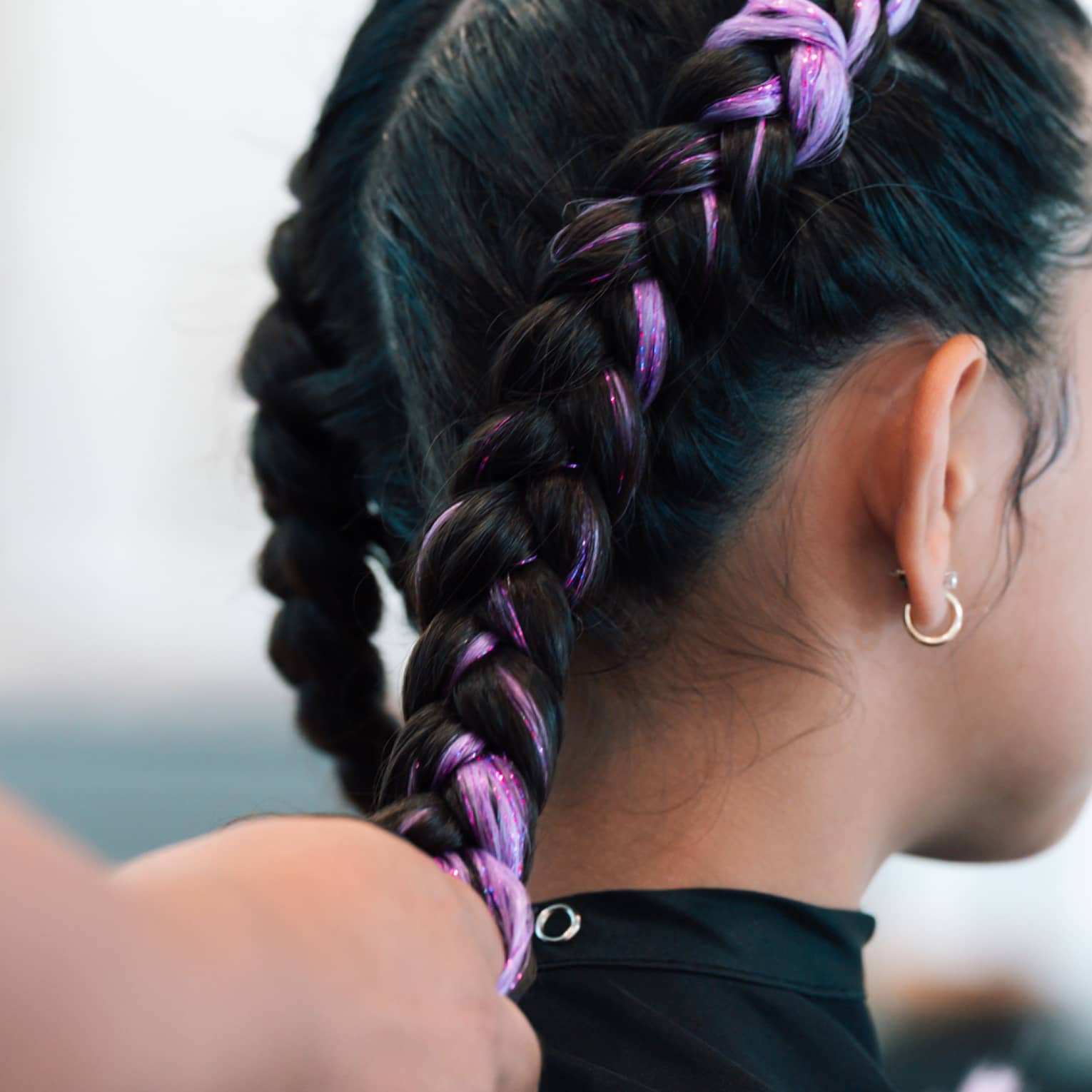 A young girl gets her hair braided with light purple interwoven color