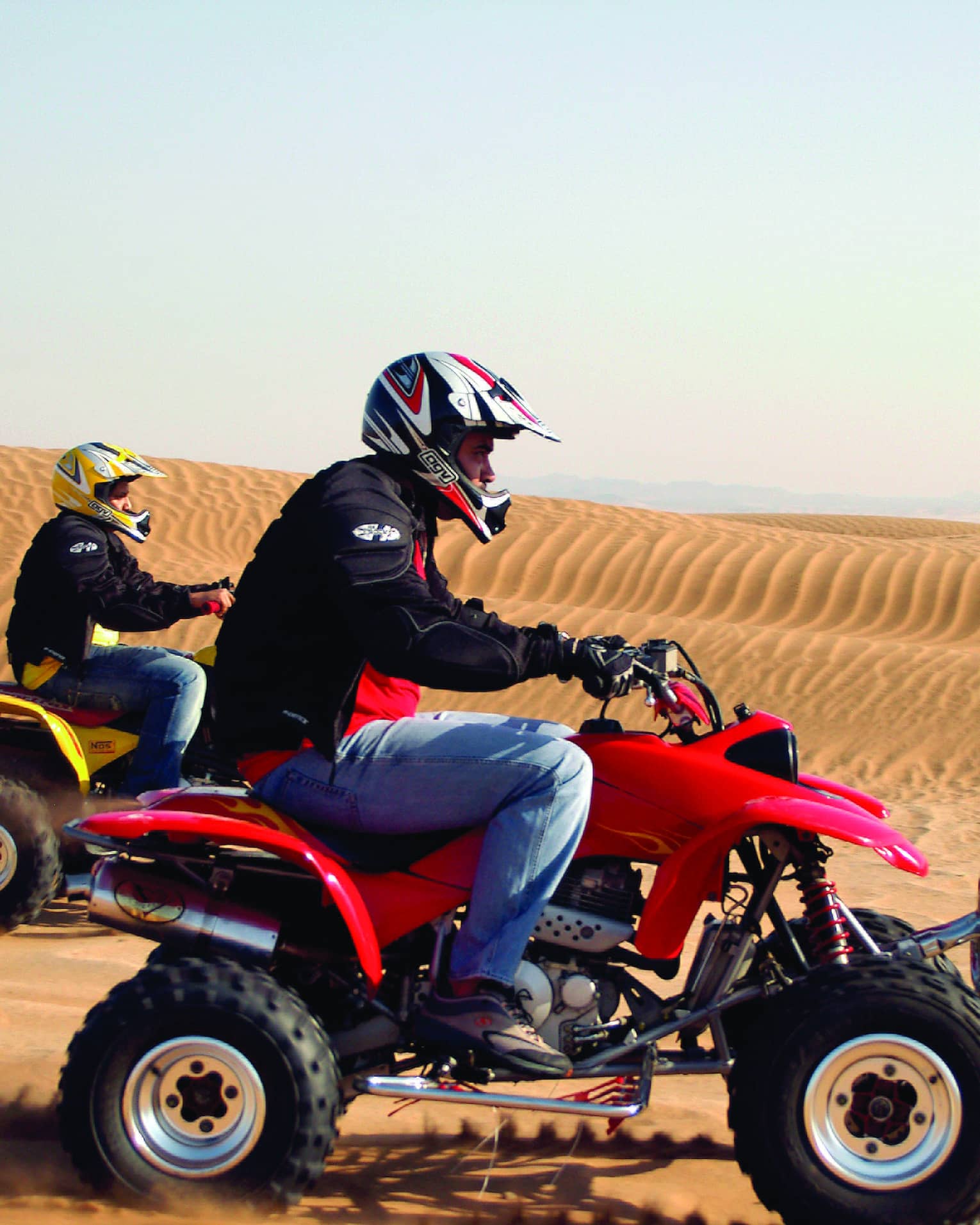 Two men riding ATVs through sand dunes in the desert