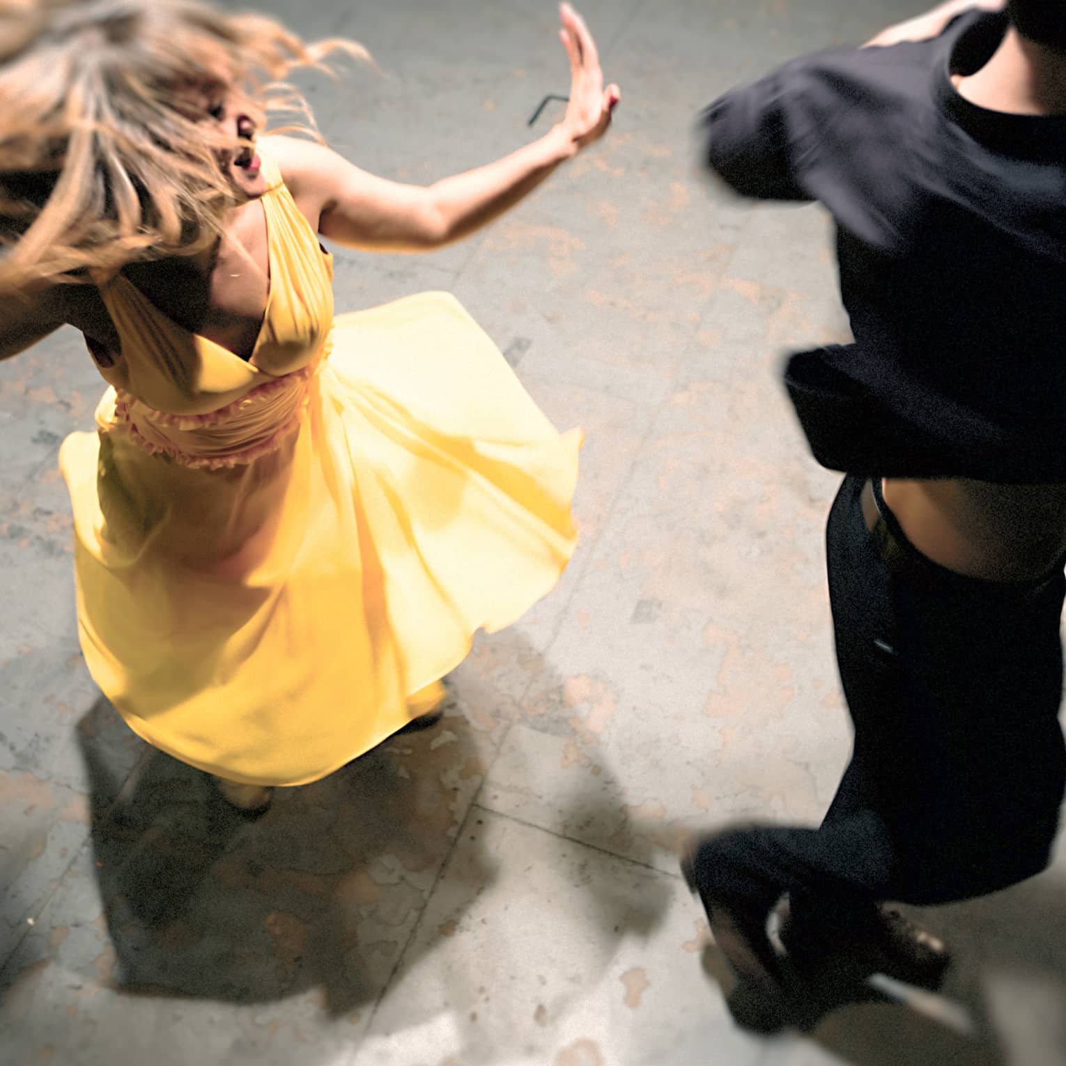 Woman in a yellow dress is spinning on the dance floor as a man wearing all black dances next to her