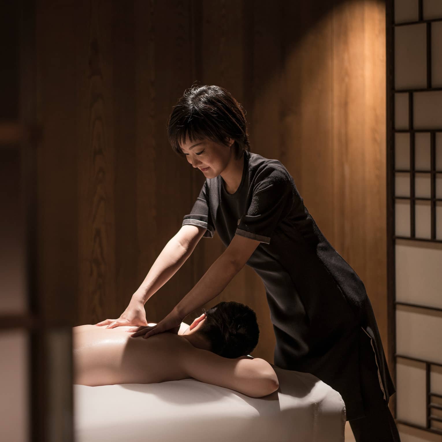 Man lies face-down on massage table as masseuse in black uniform rubs his shoulders