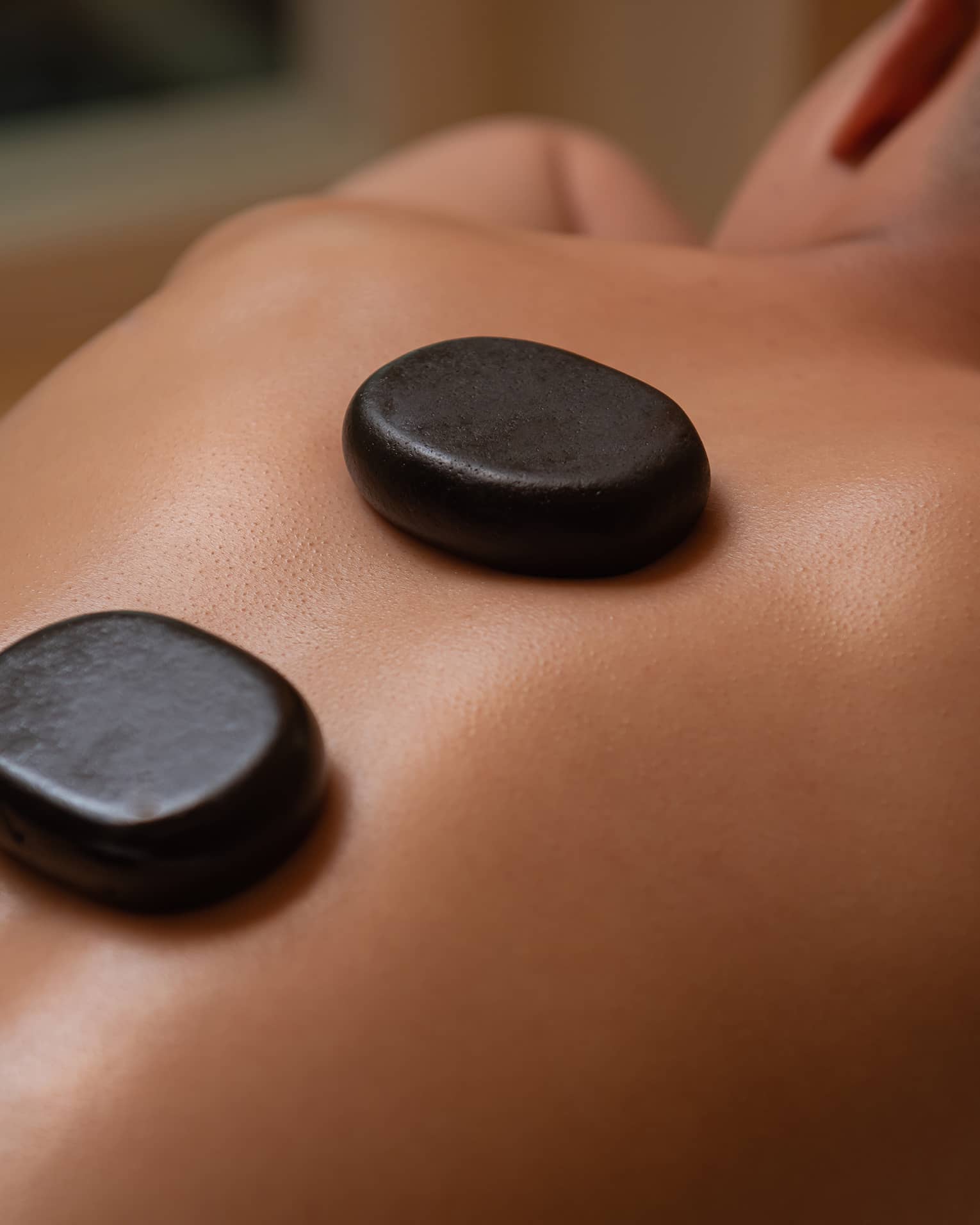 Three large black stones rest on man's bare back and spine as he lays on massage table