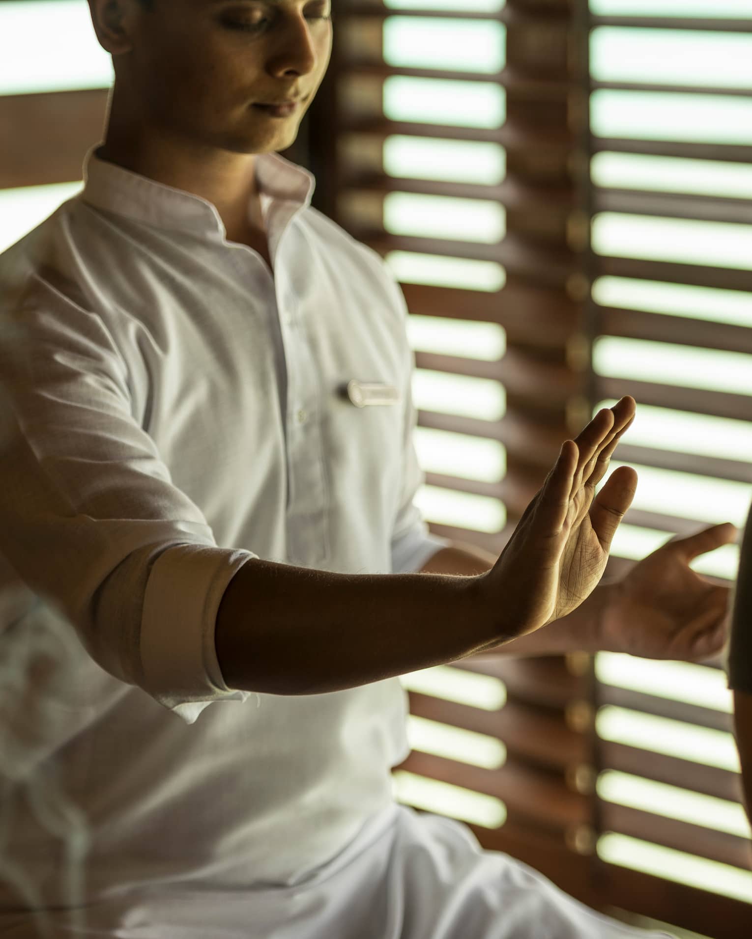 Reiki healer with eyes closed holds hand over woman's body