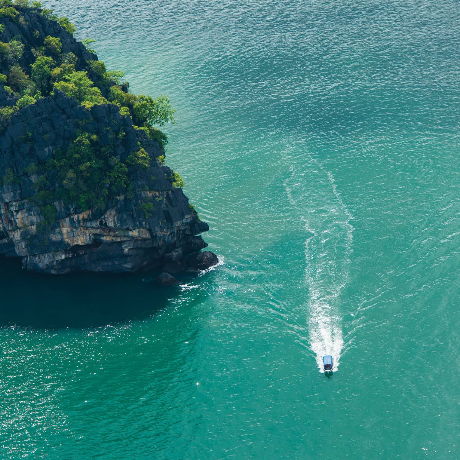 Ariel view of a boat driving through rock structures on emerald green water 
