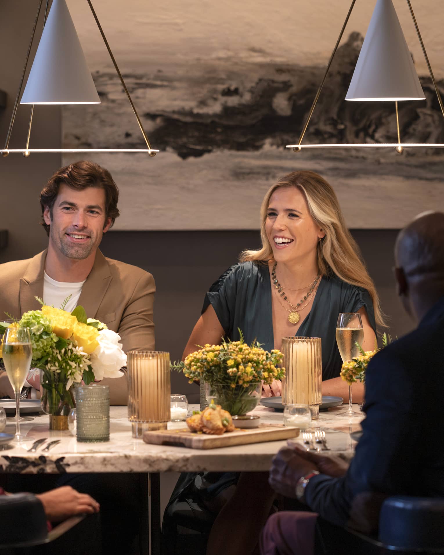 Guests sitting at a table and smiling at each other at a restaurant with overhead lighting