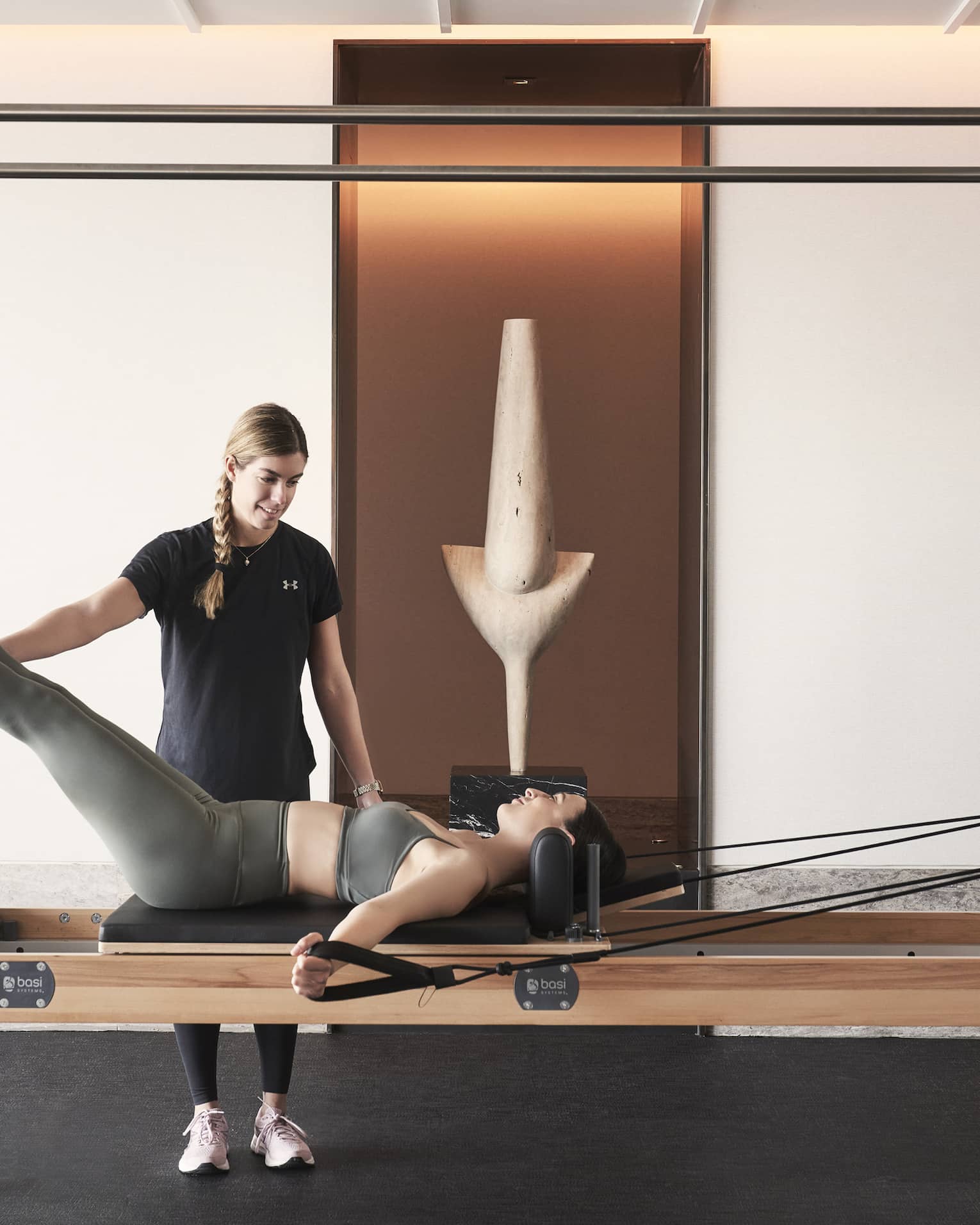 Fitness coach holds legs of woman lying and working out on a Pilates reformer