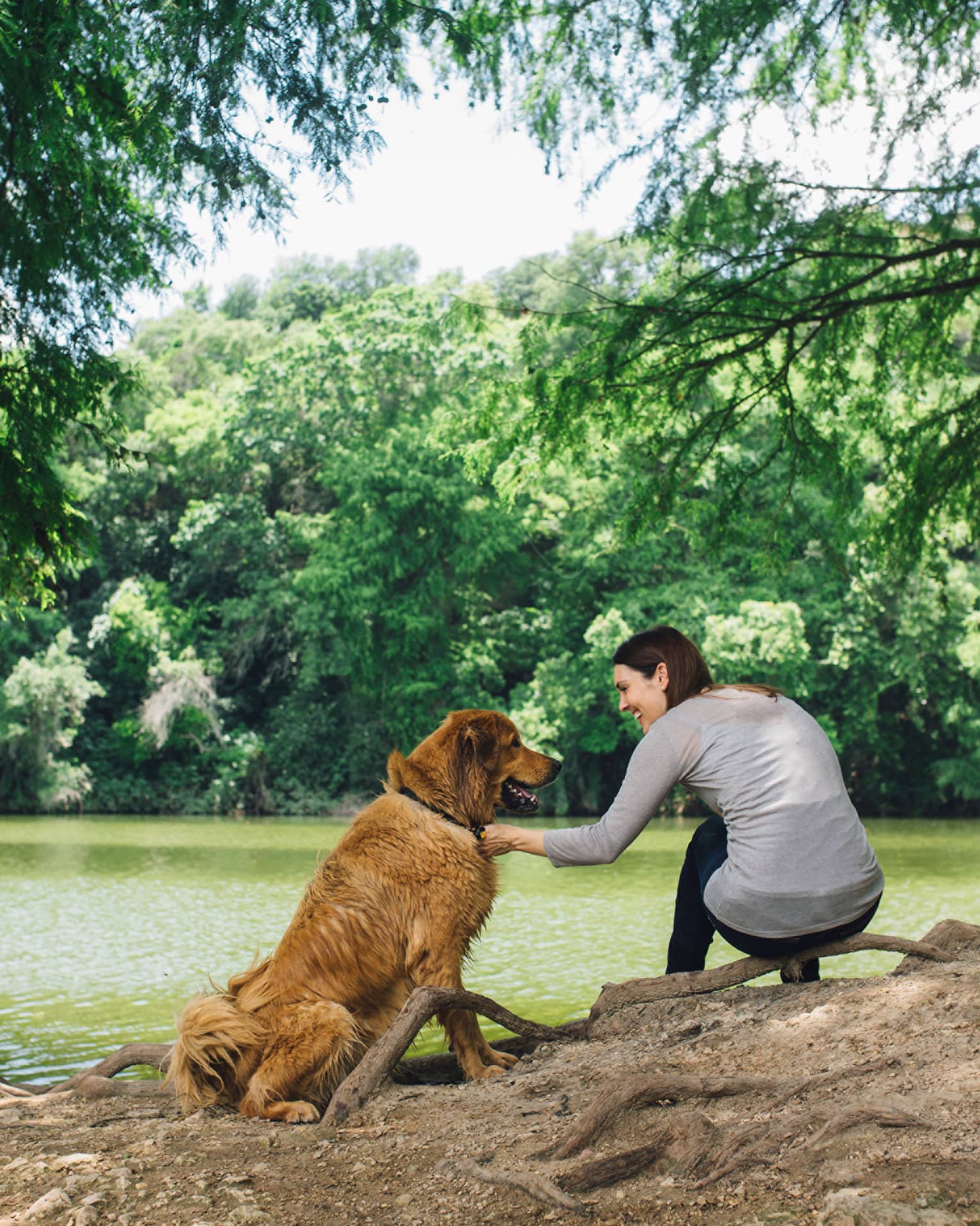 A woman pets a dog next to a lake