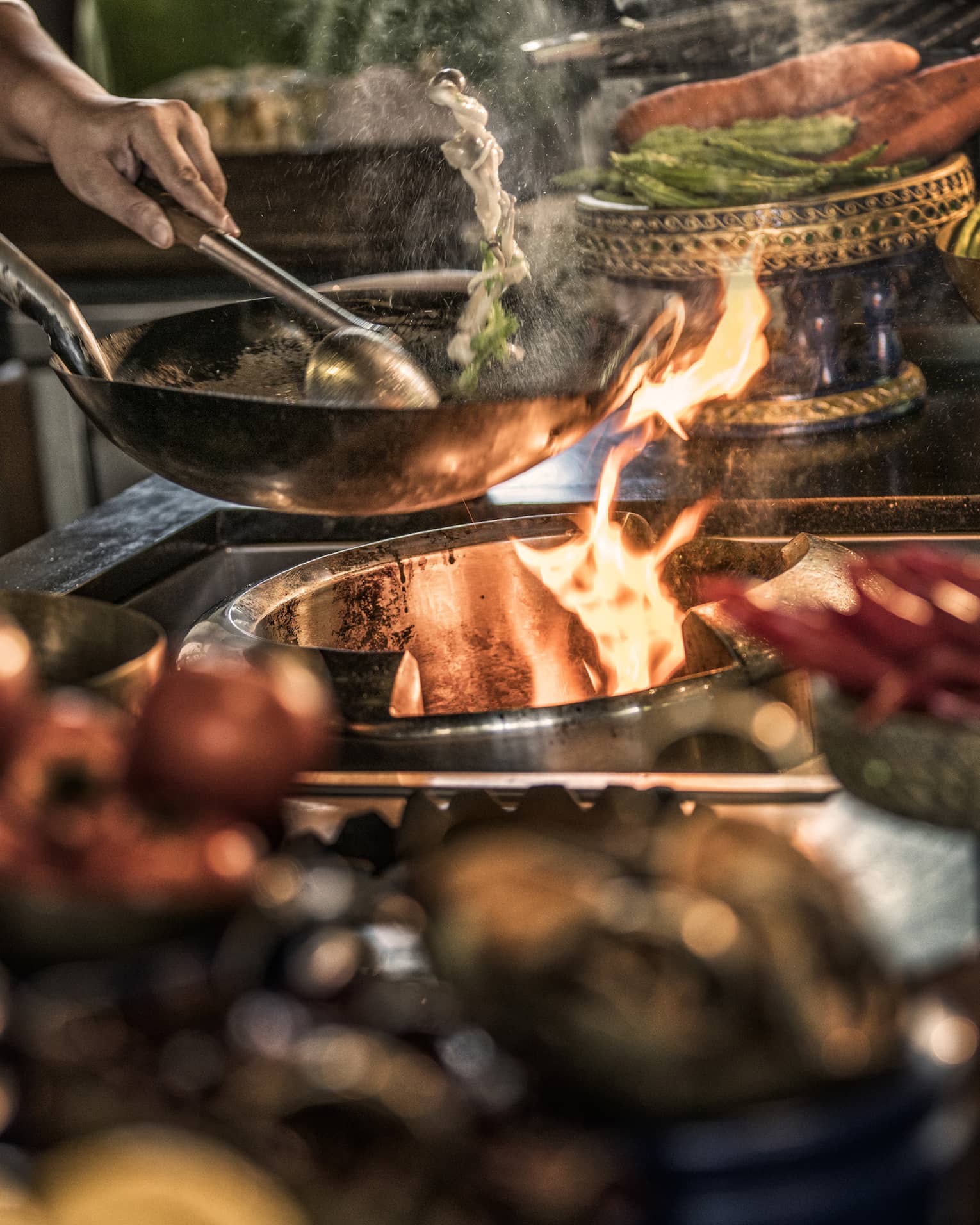 Close-up of chef stirring meals in copper pans over stove, flames
