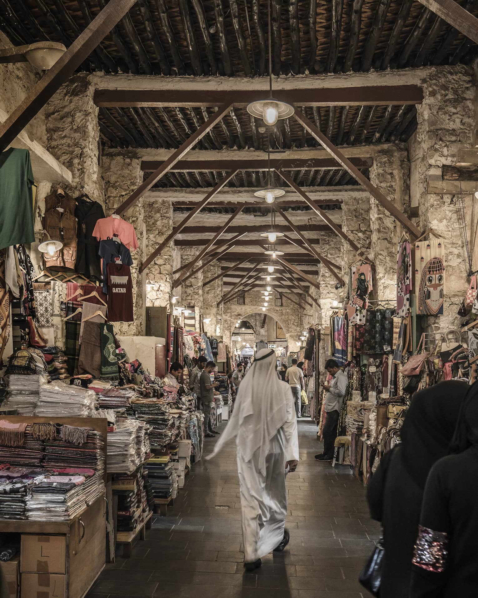 People walk past tables with textiles, clothes in indoor market