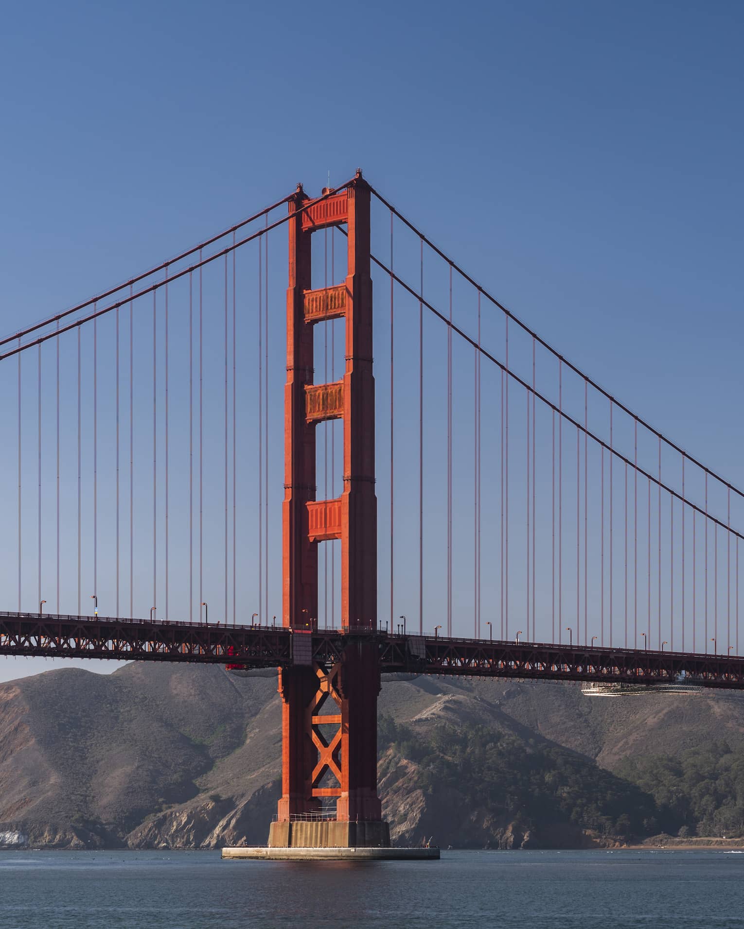 A red metal bridge with a large landmass of hills and mountains behind it.
