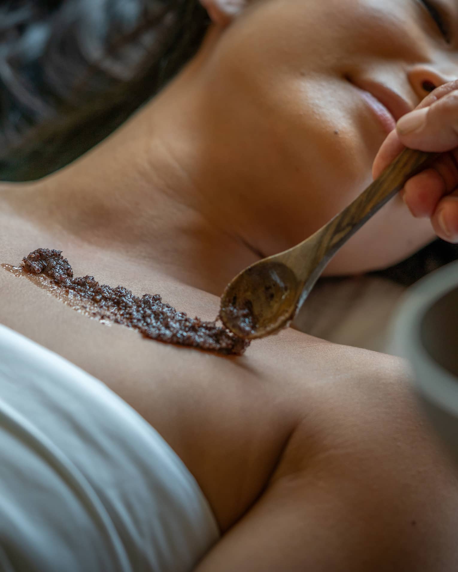 Person laying on a Spa bed while an exfoliating skin scrub is placed on their skin.