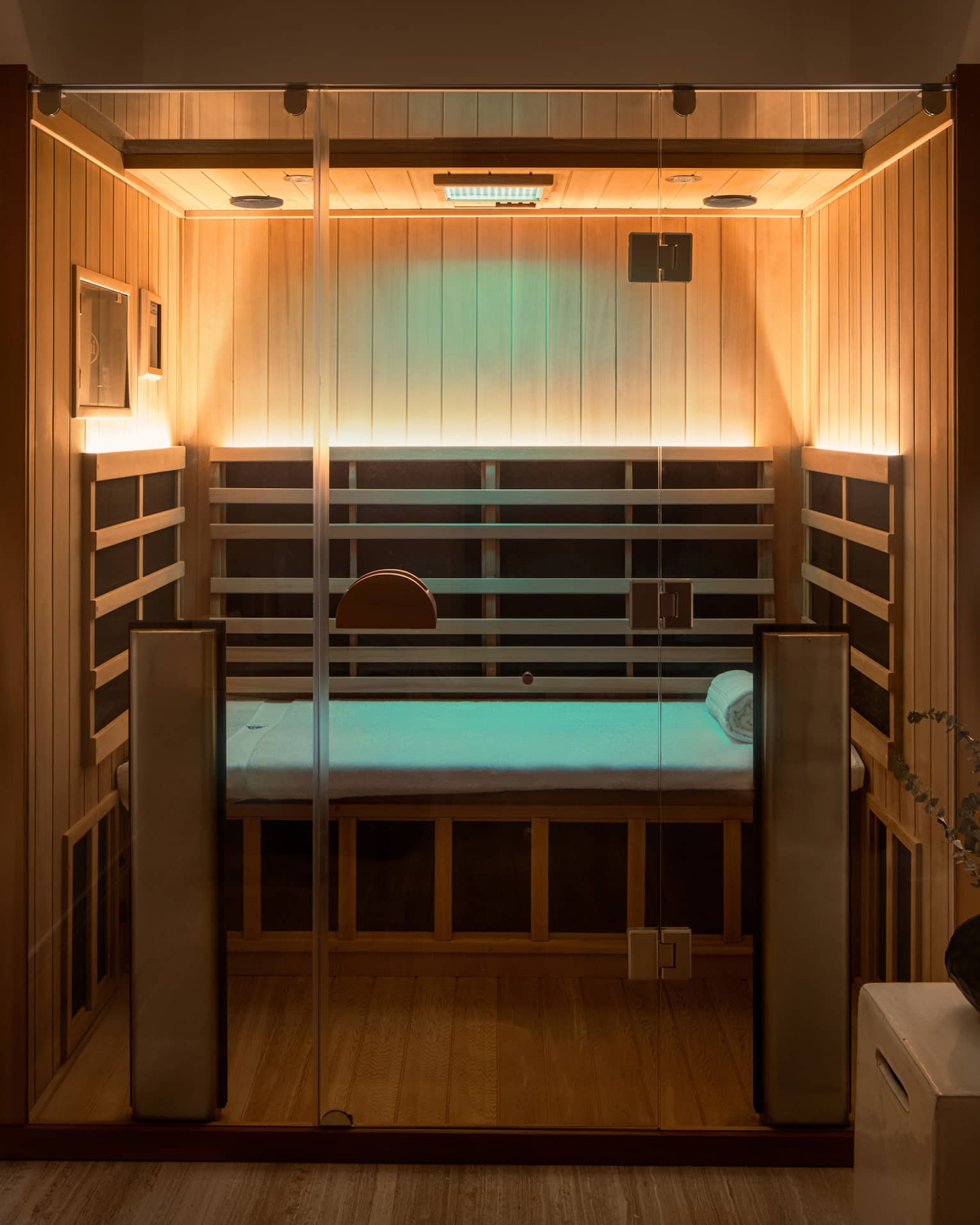 Wooden infrared sauna with lowlighting, side table with vase of eucalyptus