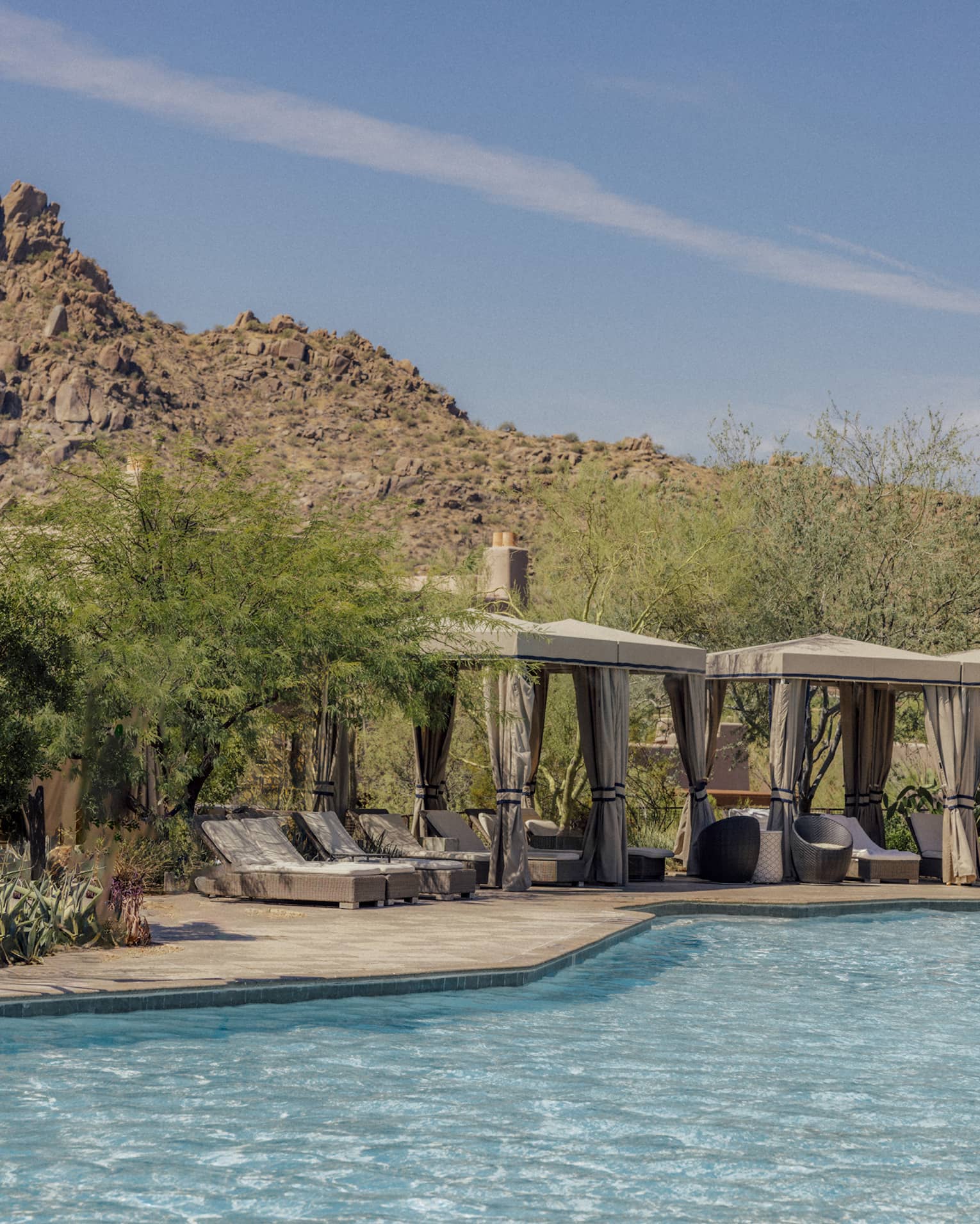 Pool with cabanas that have lounge chairs with a backdrop of the mountains.