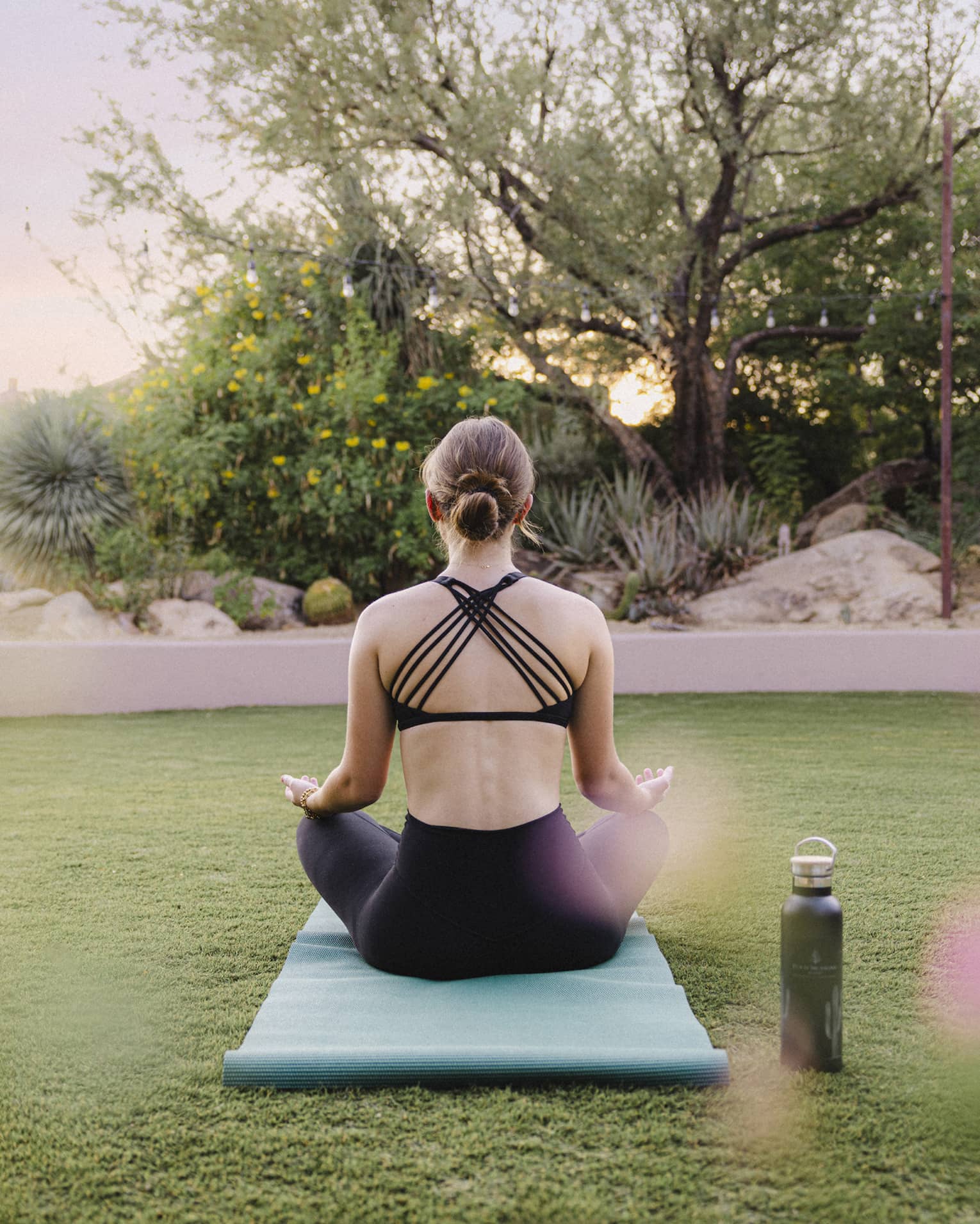 Person doing yoga outside on a blue yoga mat with a water bottle beside them.