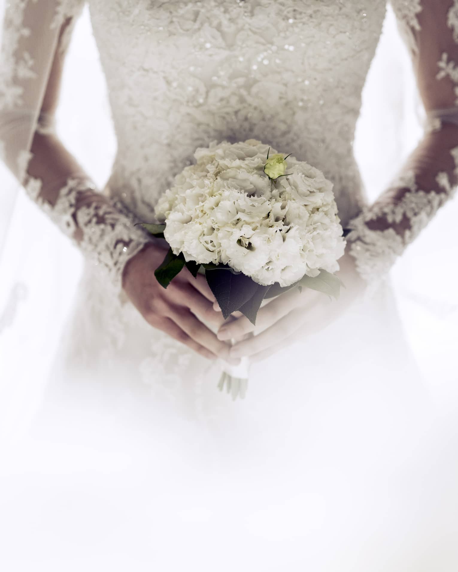 Close up on the all-white flower bouquet being held by a bride wearing a long-sleeved lace wedding gown