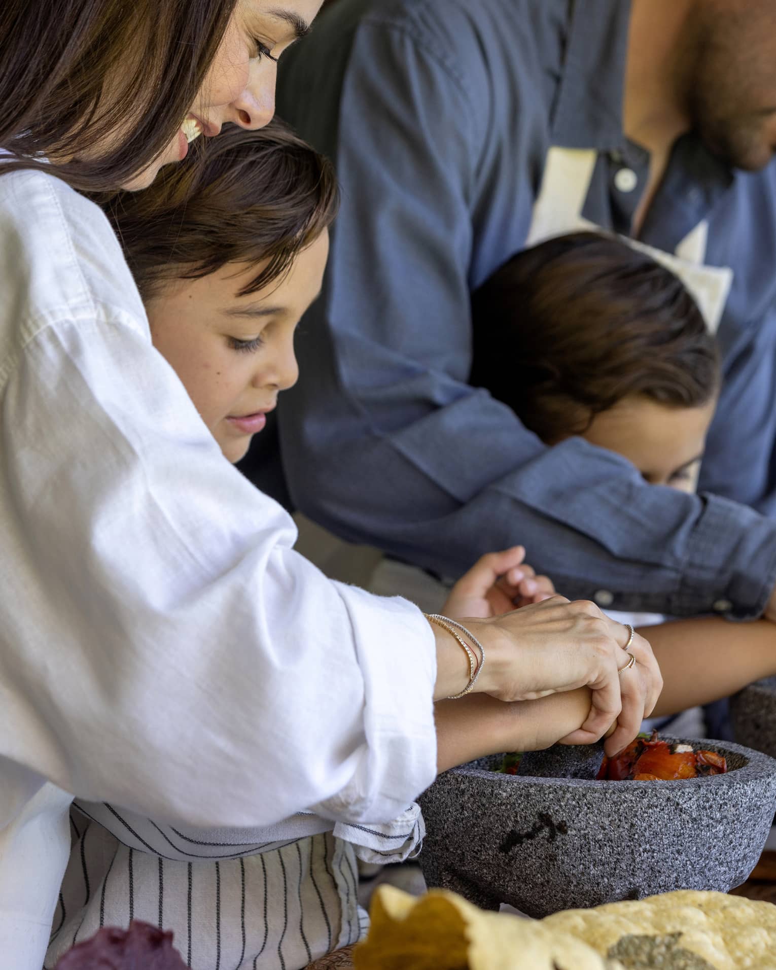 Two adult guests helping two young guests cook.