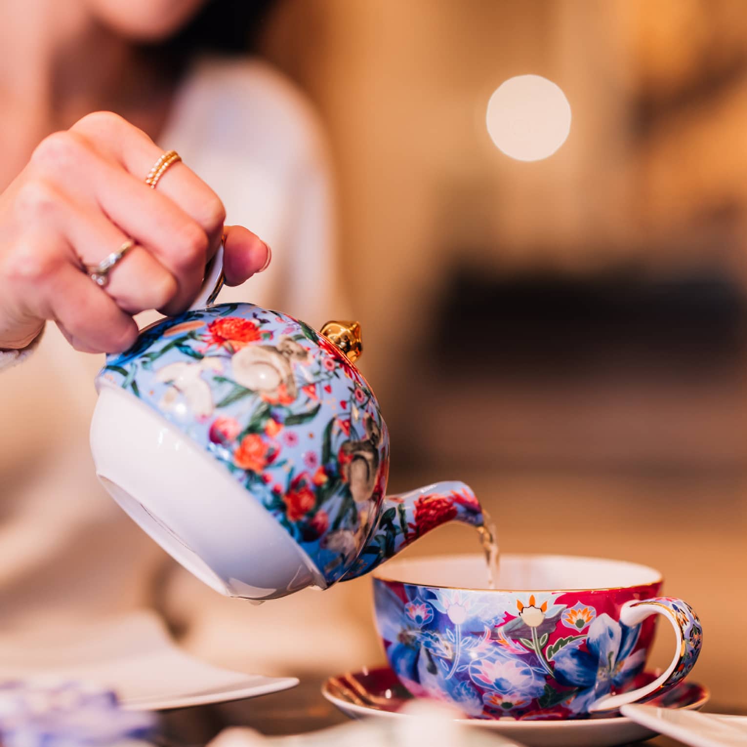 A woman pouring tea out of a colourful kettle.