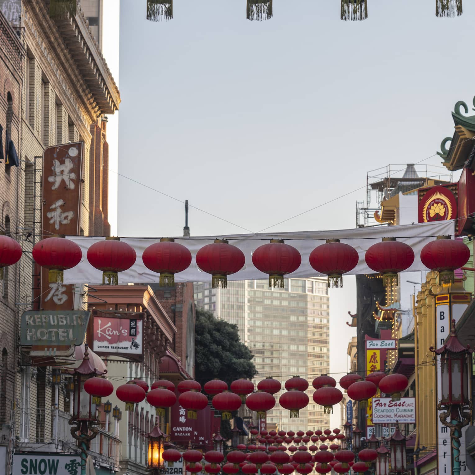 View from the bottom of a Chinatown street lined with restaurants and shops, round red lanterns strung across overhead. 