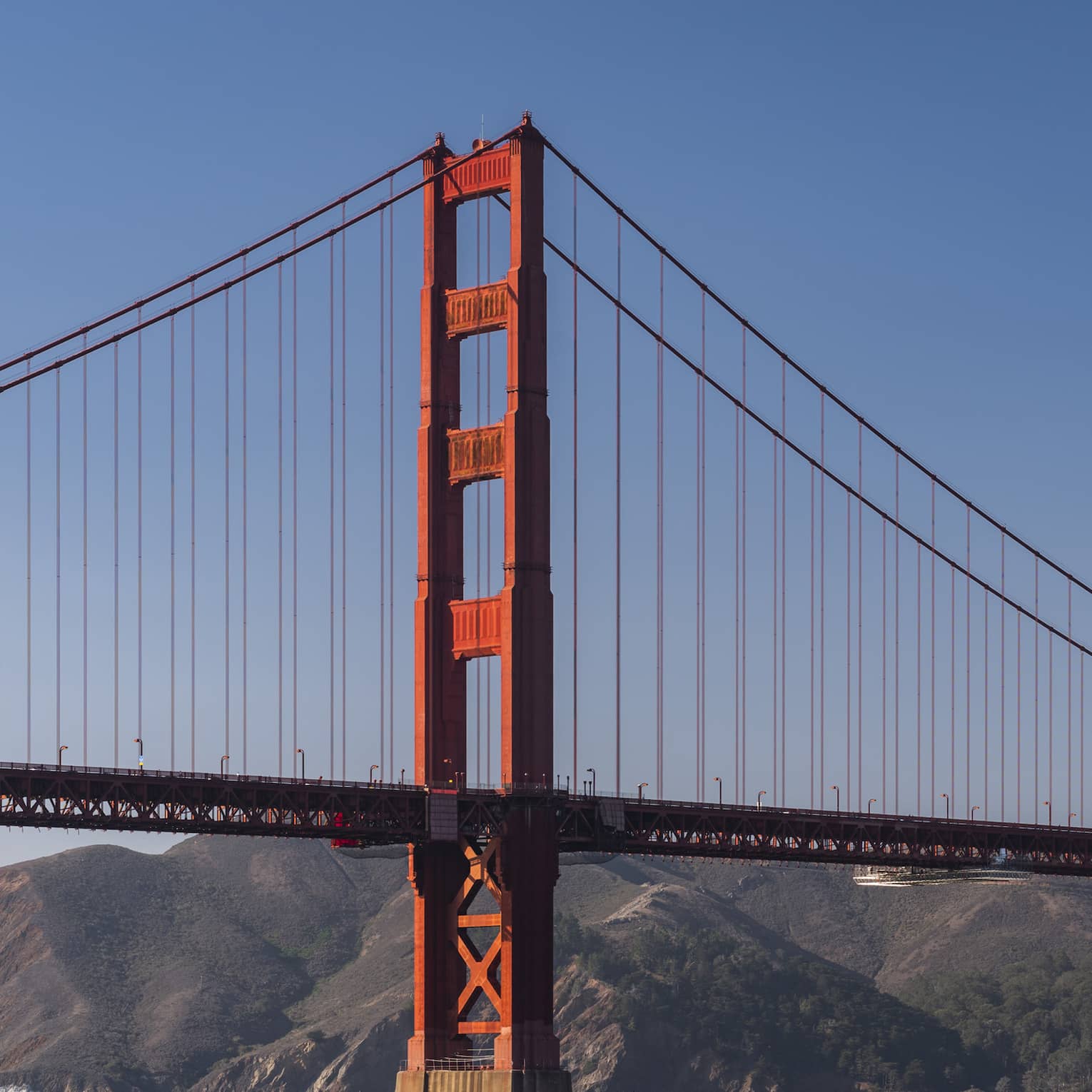 A red metal bridge with a large landmass of hills and mountains behind it.