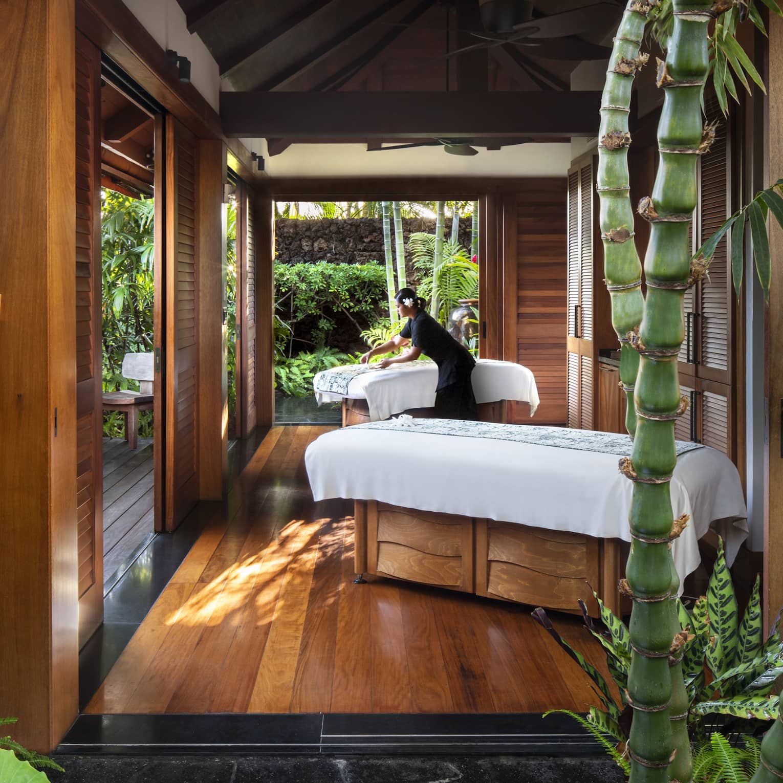 Spa staff spreads sheet on couples massage beds on open-air pavilion 