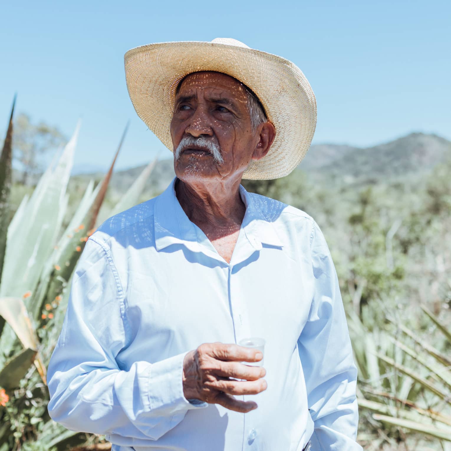 Person wearing a hat and a blue button down shirt standing outside.